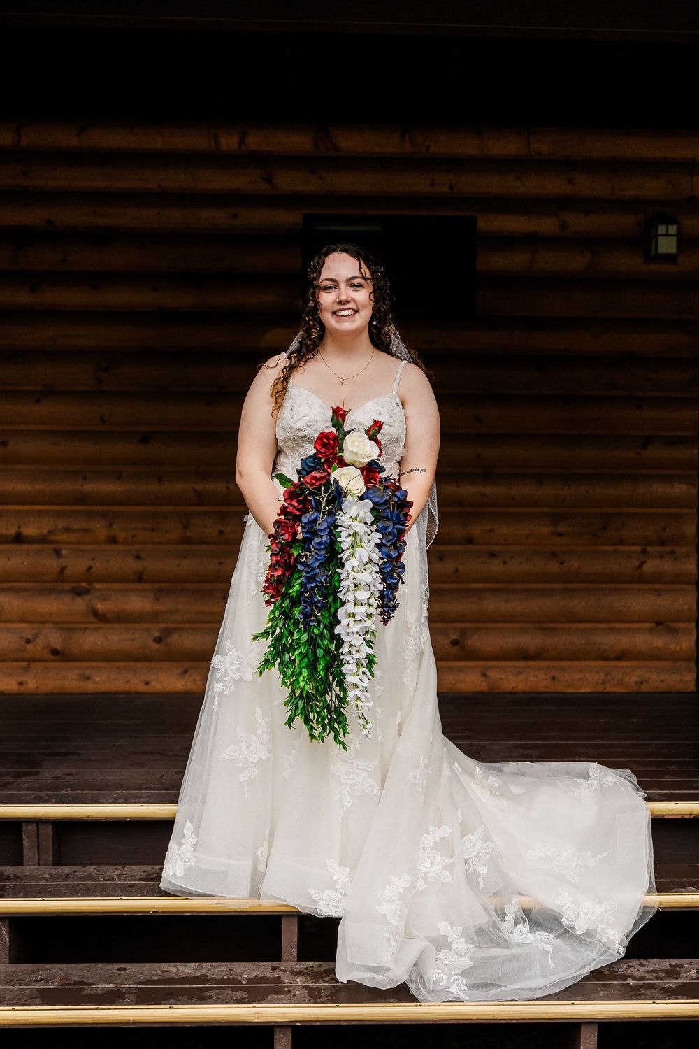 A bride in a flowing white dress holds a cascading bouquet of red and purple flowers.