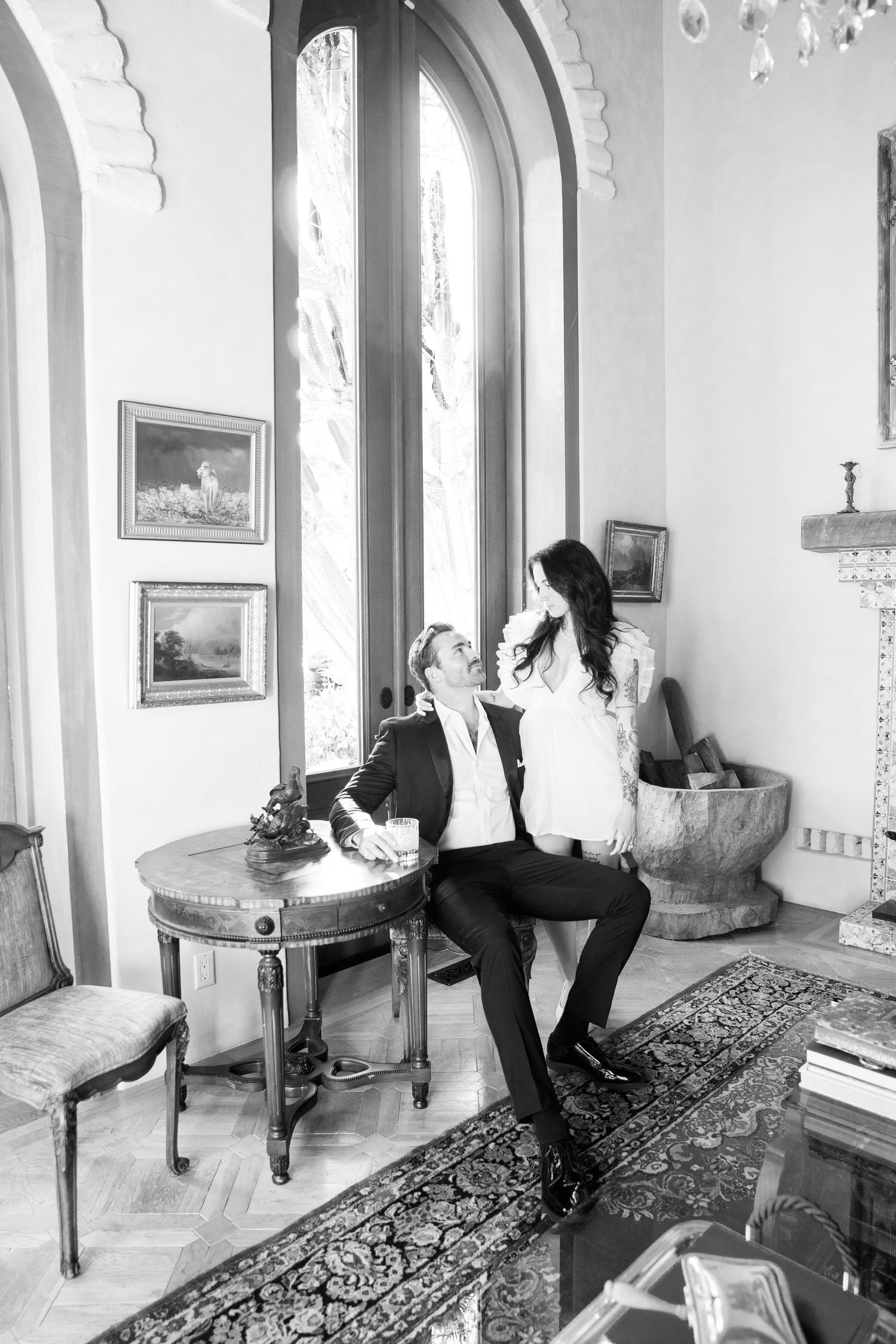 A romantic black and white moment shared in an elegant room with arched windows and antique furnishings.