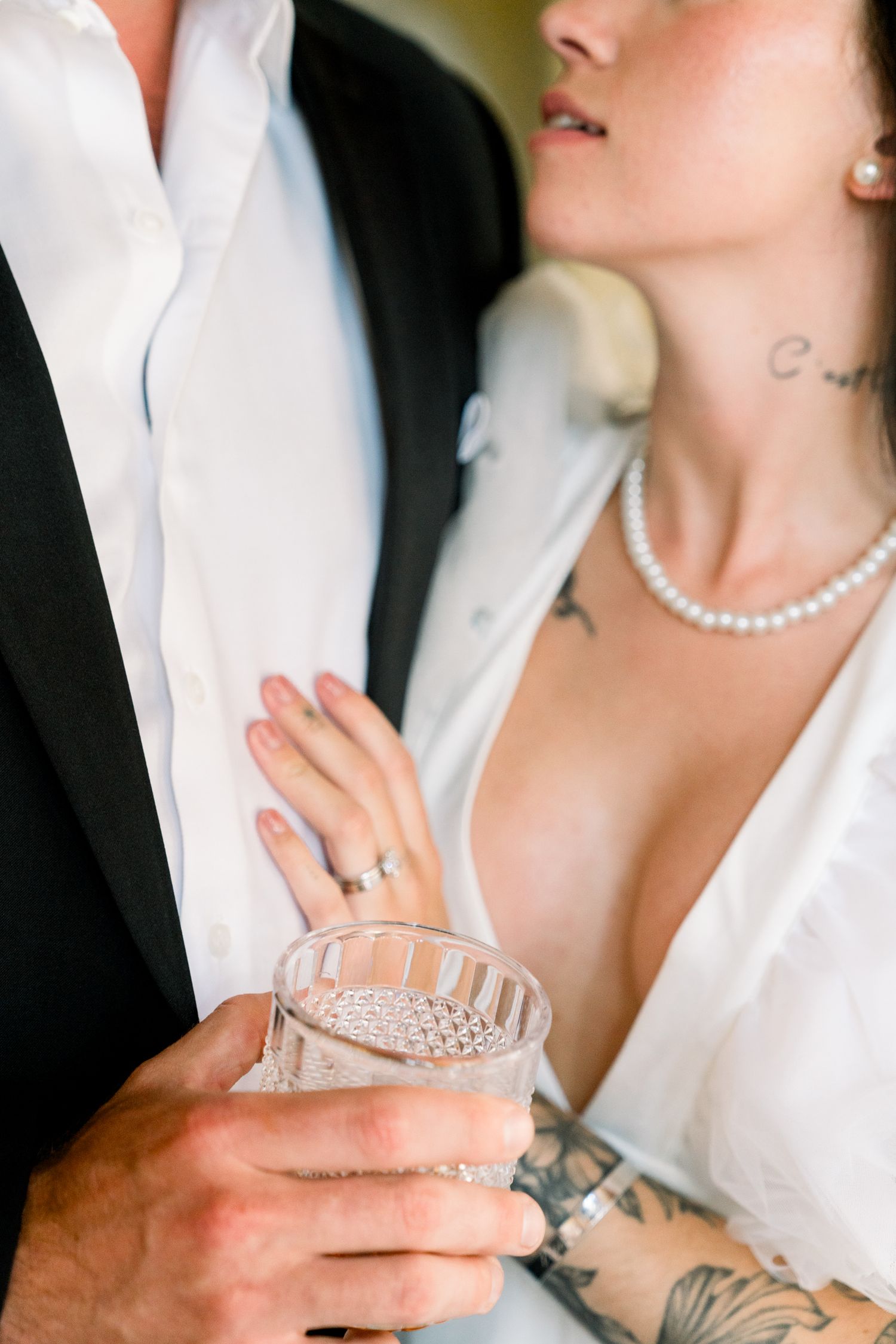 Close-up of hands holding crystal glass with pearl necklace and white formal attire in wedding setting.