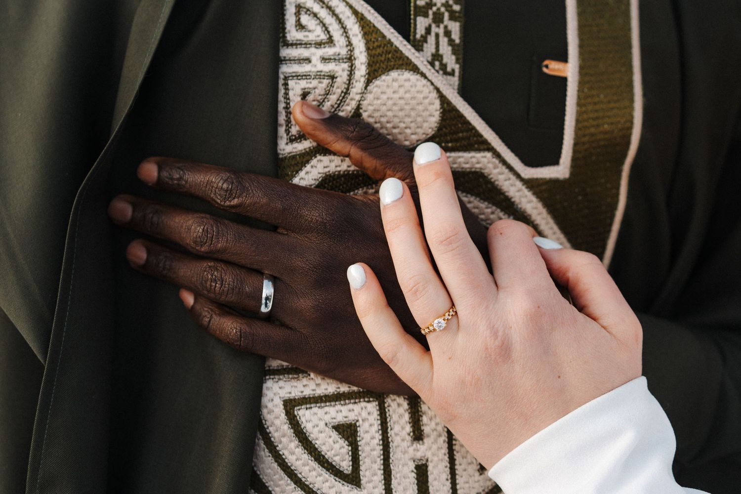 Two hands with wedding rings rest together against a fabric with geometric patterns in black and white.