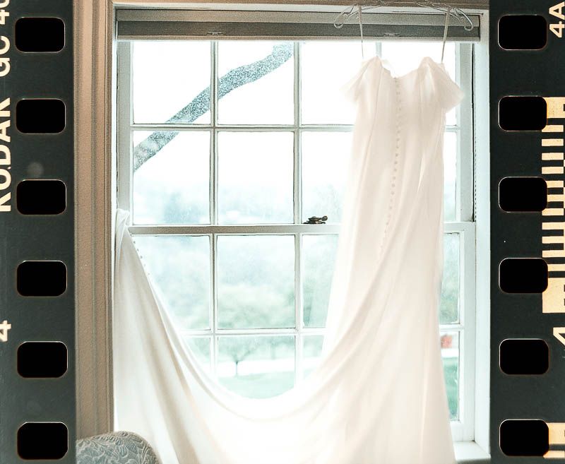 White wedding dress hangs by a window, silhouetted on a frame of 35mm Film Fox Chapel Christ First Church Near Pittsburgh PA photography.