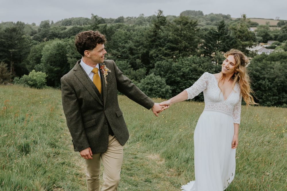 Couple spins joyfully through a green field during their outdoor wedding photoshoot.