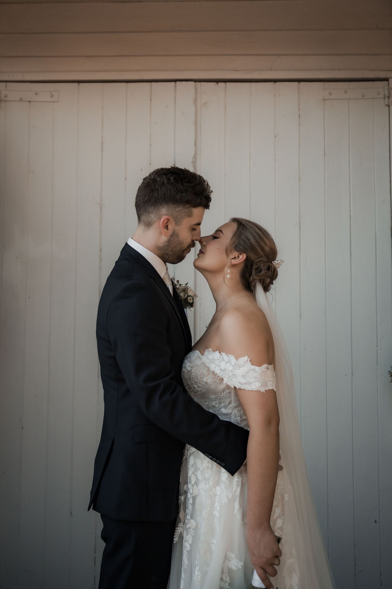 An intimate wedding portrait against a white wooden wall background.