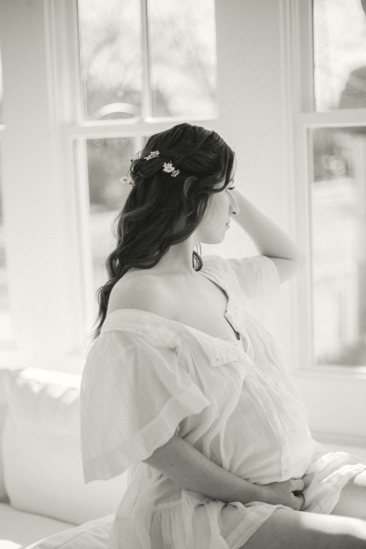 Black and white photo capturing a serene moment with flowing white fabric and delicate flowers in long dark hair.
