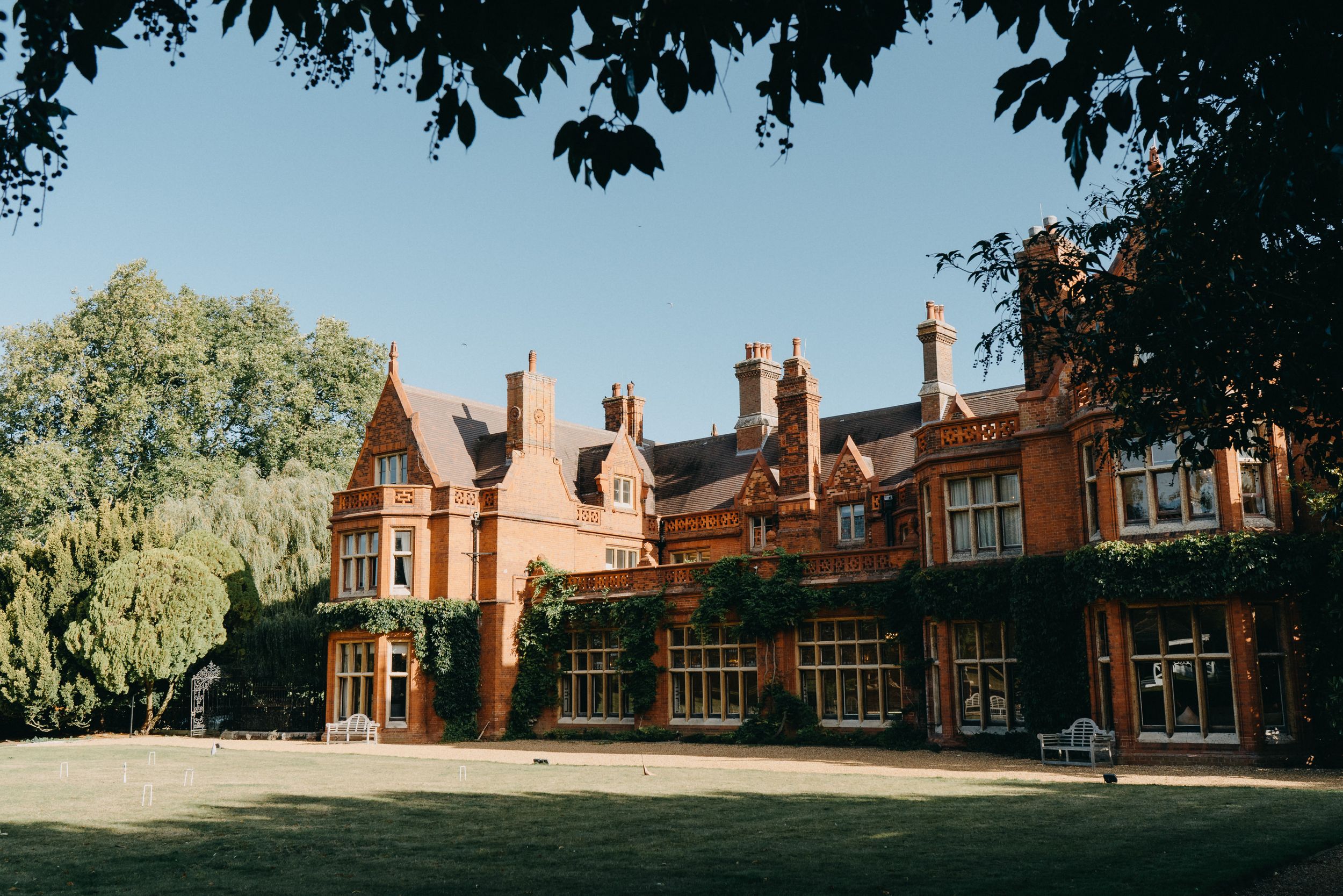 Historic red brick Victorian mansion Holmewood Hall with ornate architectural details and tall chimneys stands against a bright blue sky.