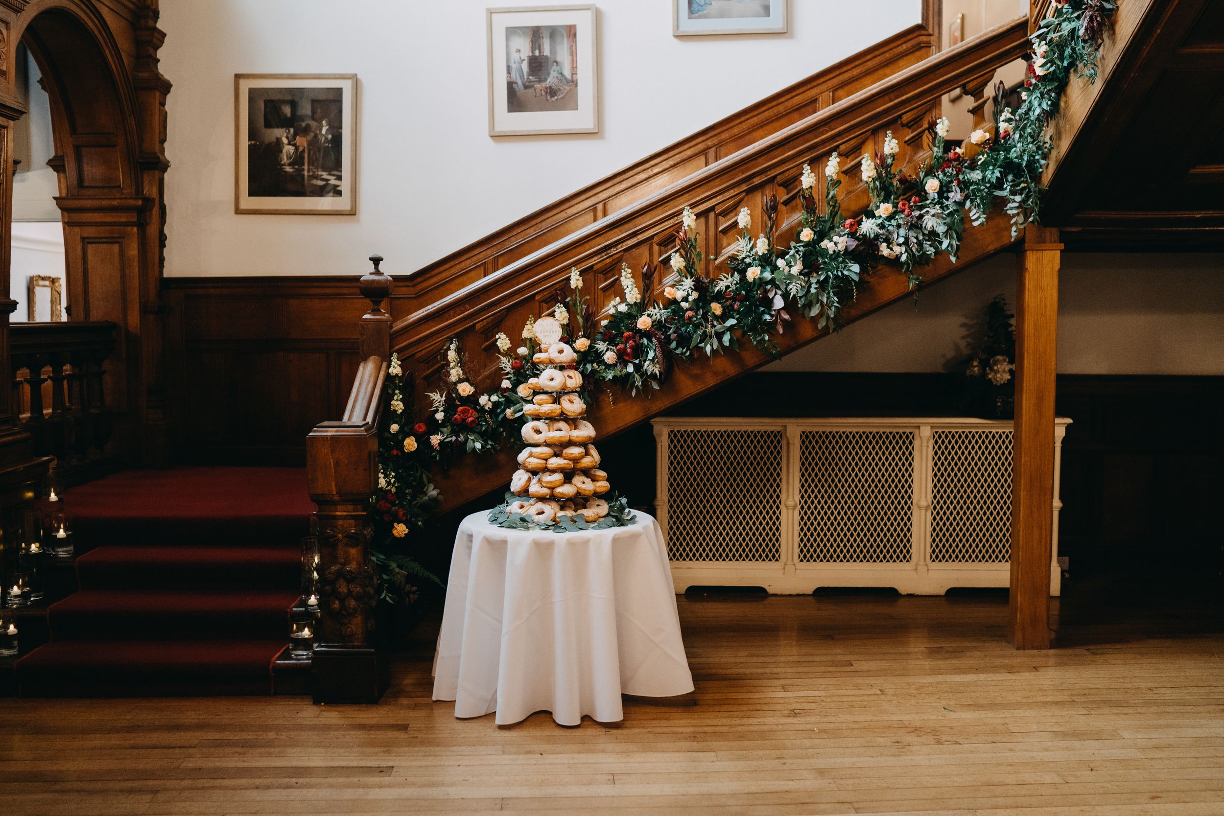 Croquembouche dessert tower displayed on white tablecloth near elegant wooden staircase adorned with holiday garland.