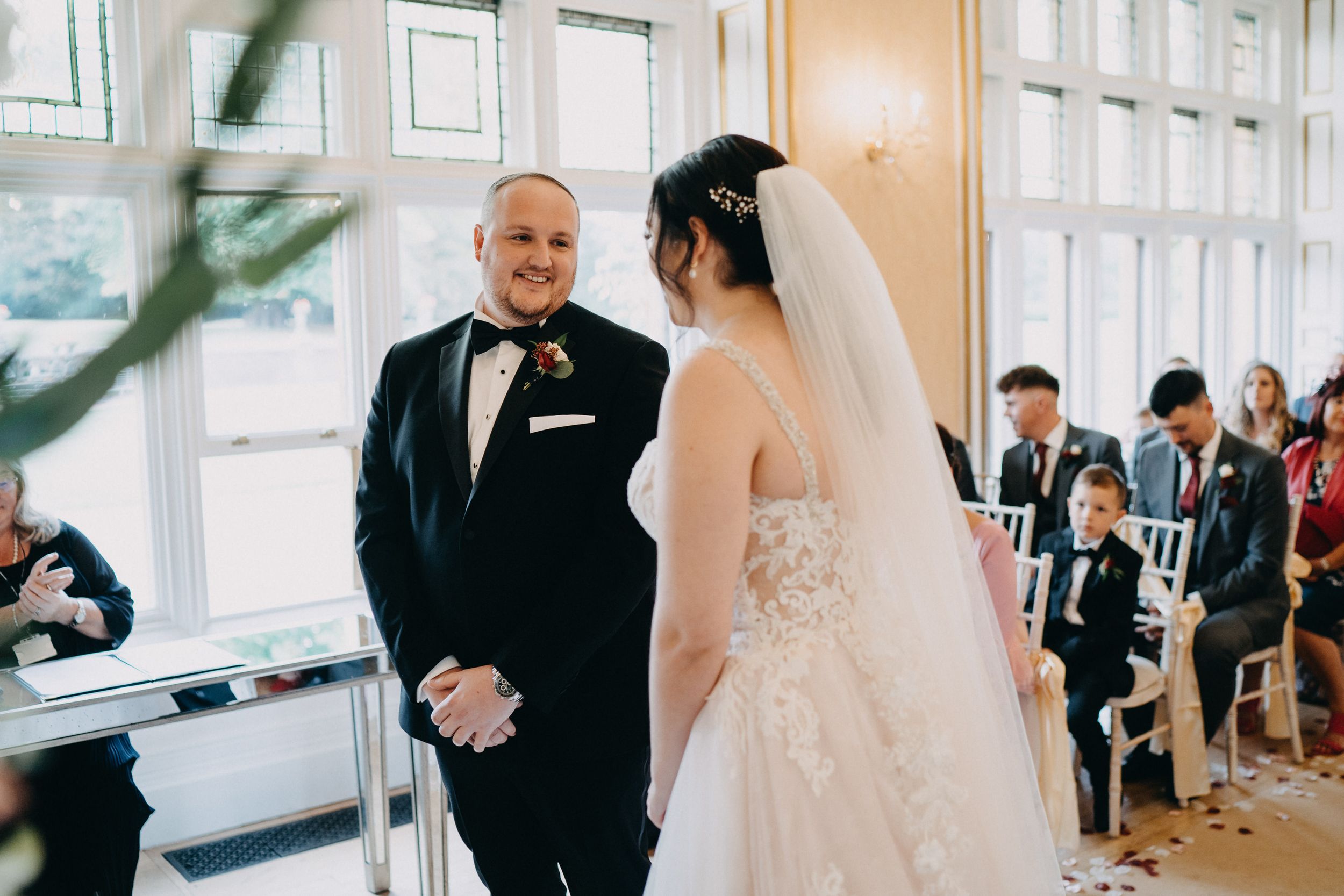 A bride and groom share a joyful moment during their wedding ceremony in a bright, modern venue with guests seated behind them.