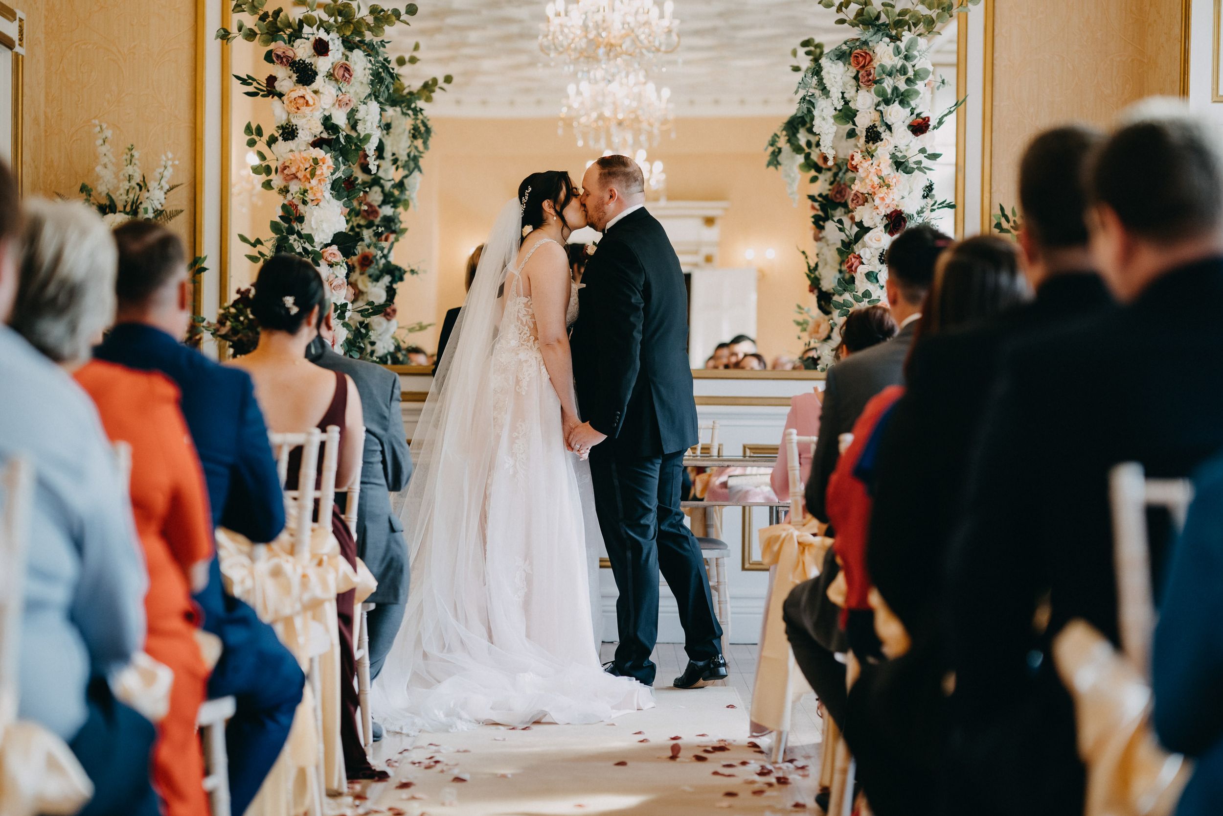 Wedding ceremony at Holmewood Hall surrounded by floral archway and seated guests.