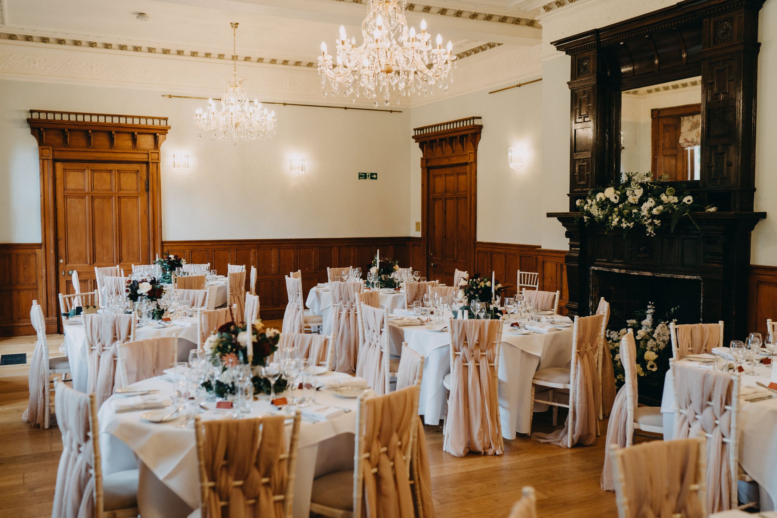Elegant wedding reception at Holmewood Hall with white-draped tables, golden chairs, and ornate crystal chandeliers.