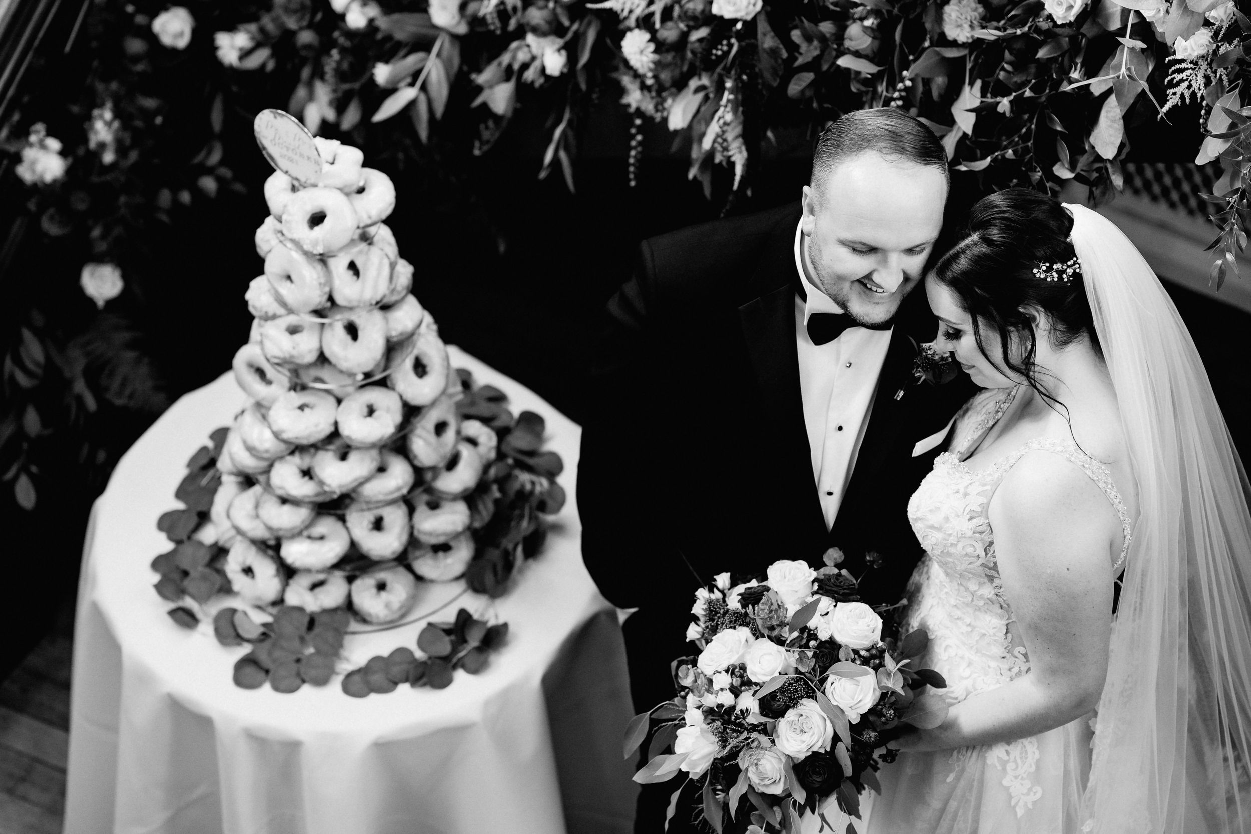 Black and white wedding photograph showing a couple next to an elaborate Croquembouche dessert tower at their reception.