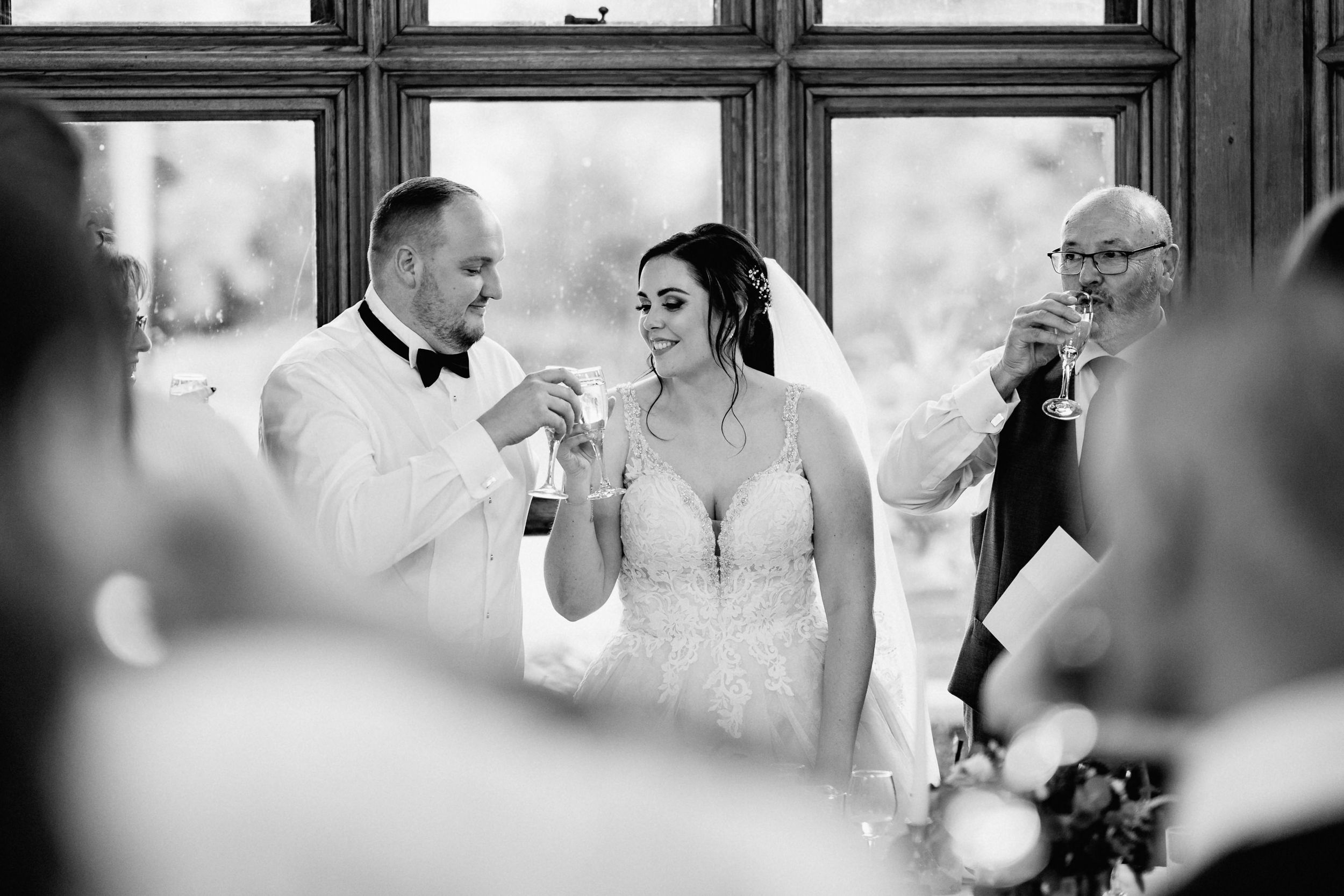 A black and white photo of guests raising champagne glasses in a celebratory toast during an elegant wedding reception.