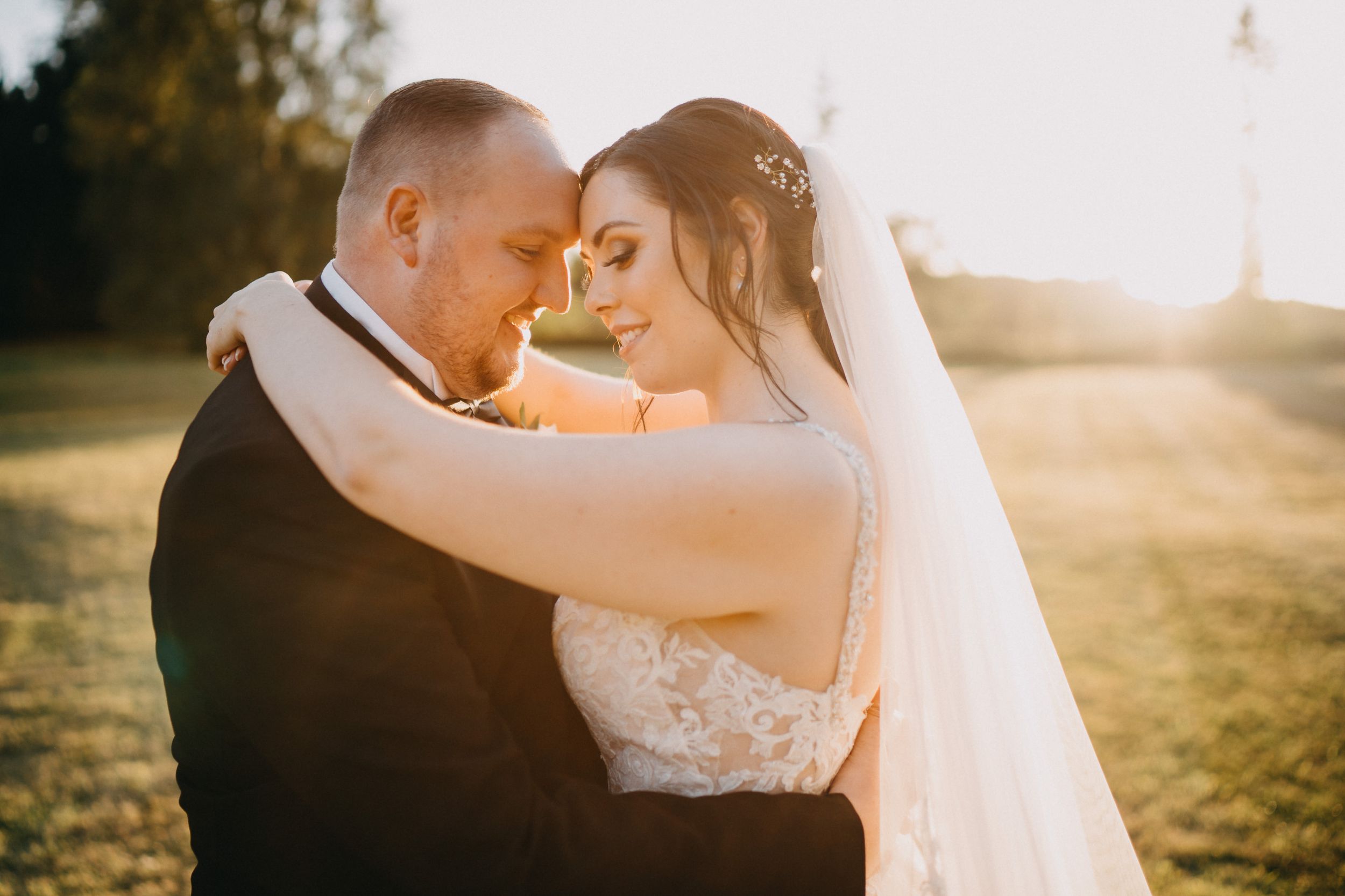 A couple embraces during golden hour at Holmewood Hall in an outdoor wedding setting with warm sunlight and a flowing veil.
