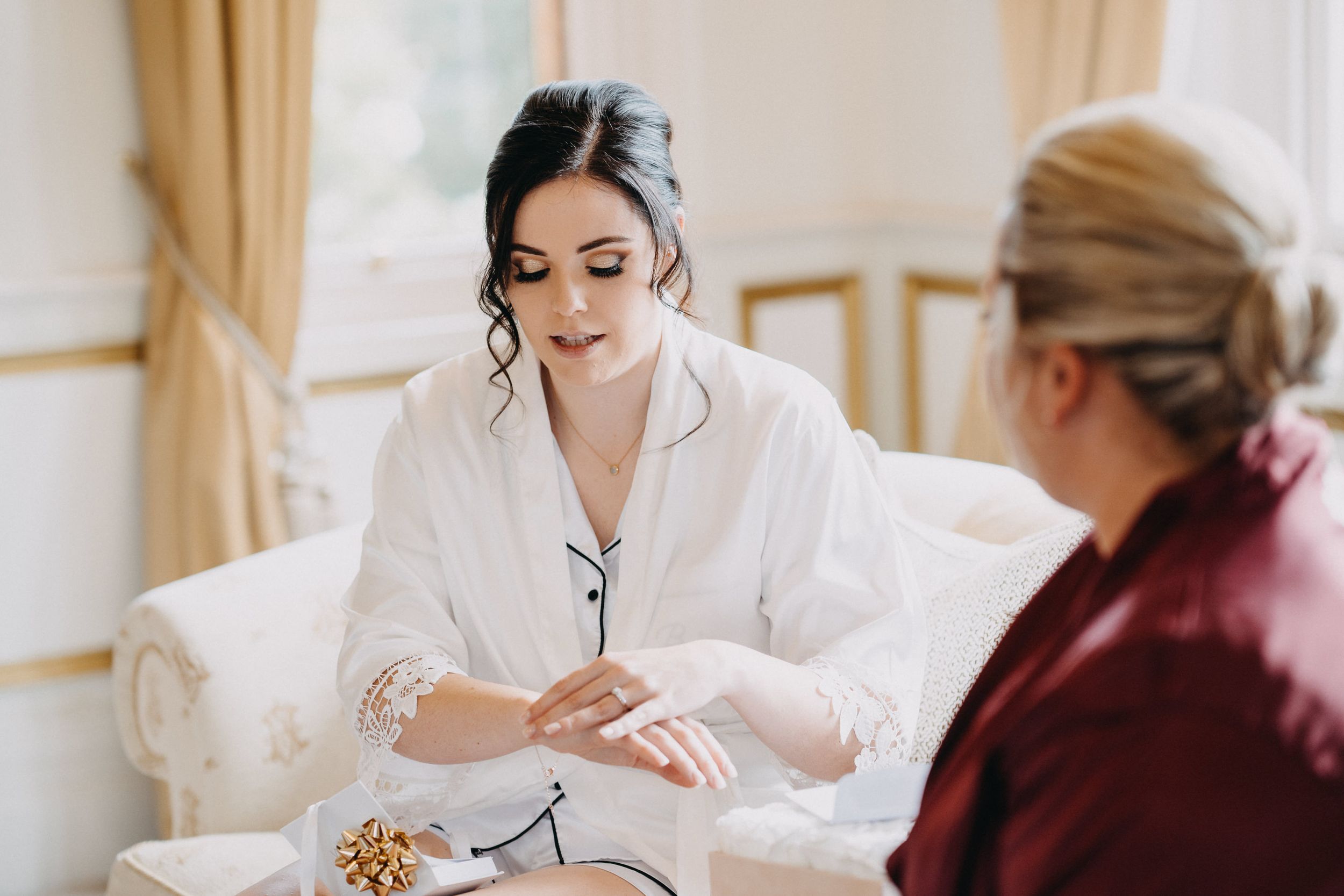 Two people in an elegant room having a discussion while seated, with one wearing a white robe and the other in burgundy.