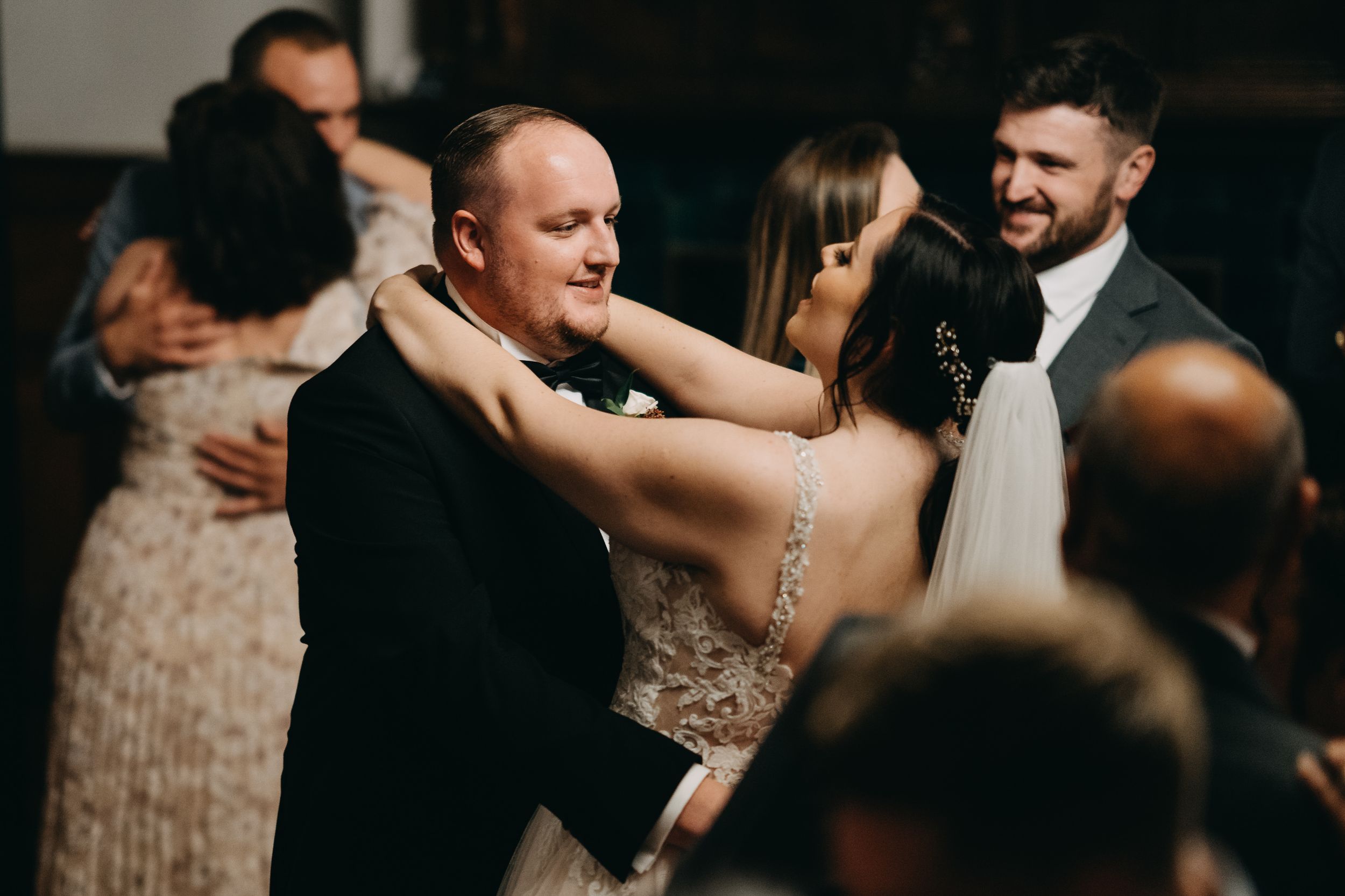 Wedding reception guests dancing together in a dimly lit venue during a celebration.
