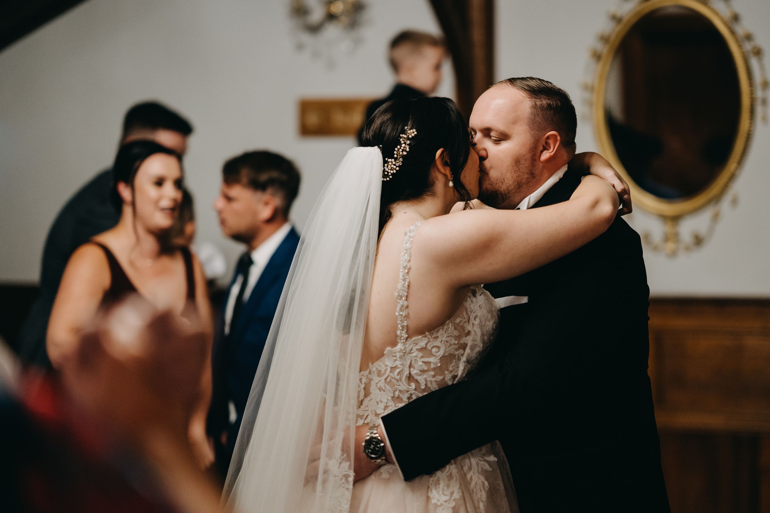 A newlywed couple shares their first kiss during an intimate indoor wedding ceremony.