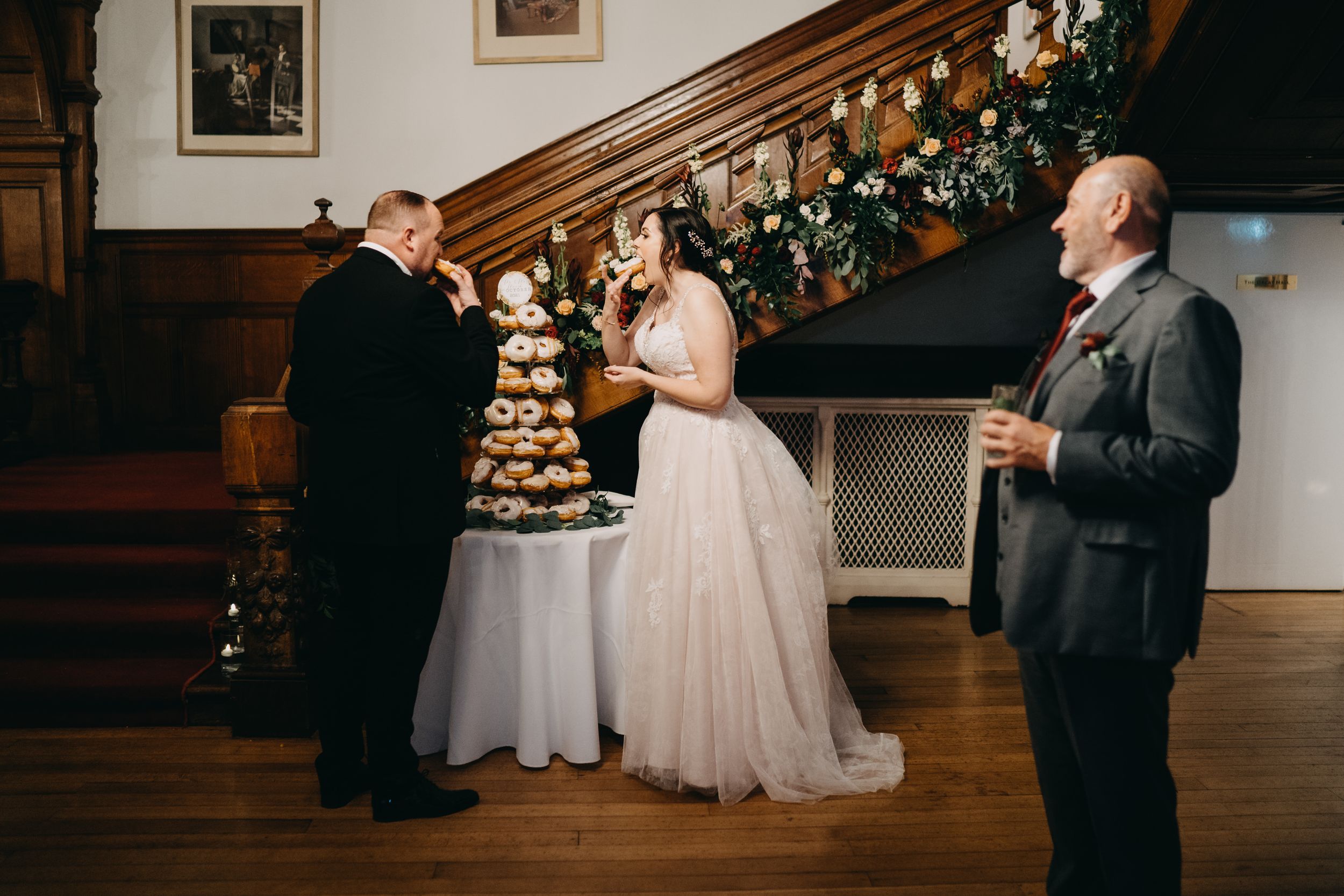 Wedding couple cutting their elegant chocolate wedding cake on display in a wood-paneled reception room with holiday garland decor.