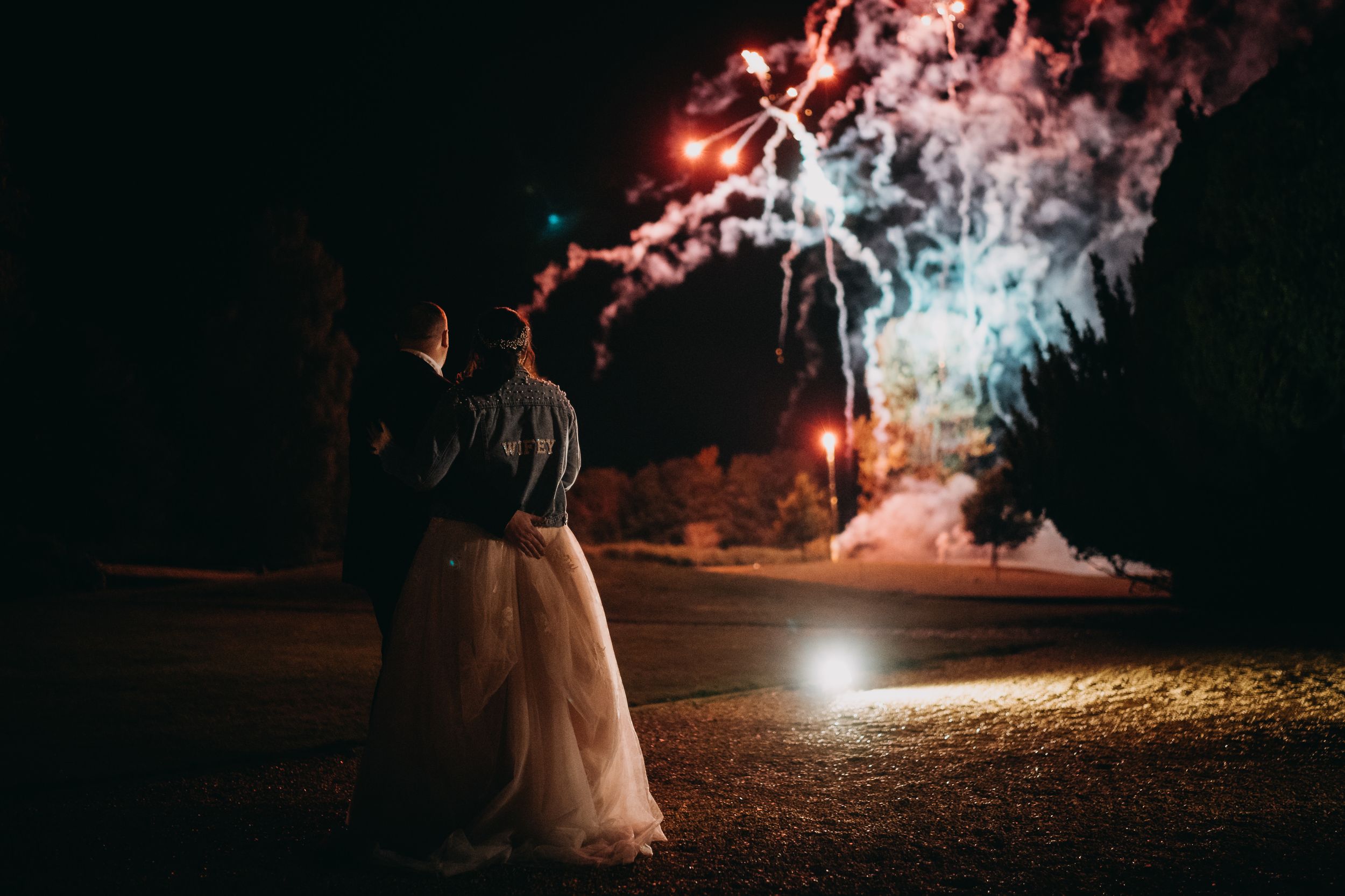 A couple watches colorful fireworks illuminate the night sky during an outdoor celebration.