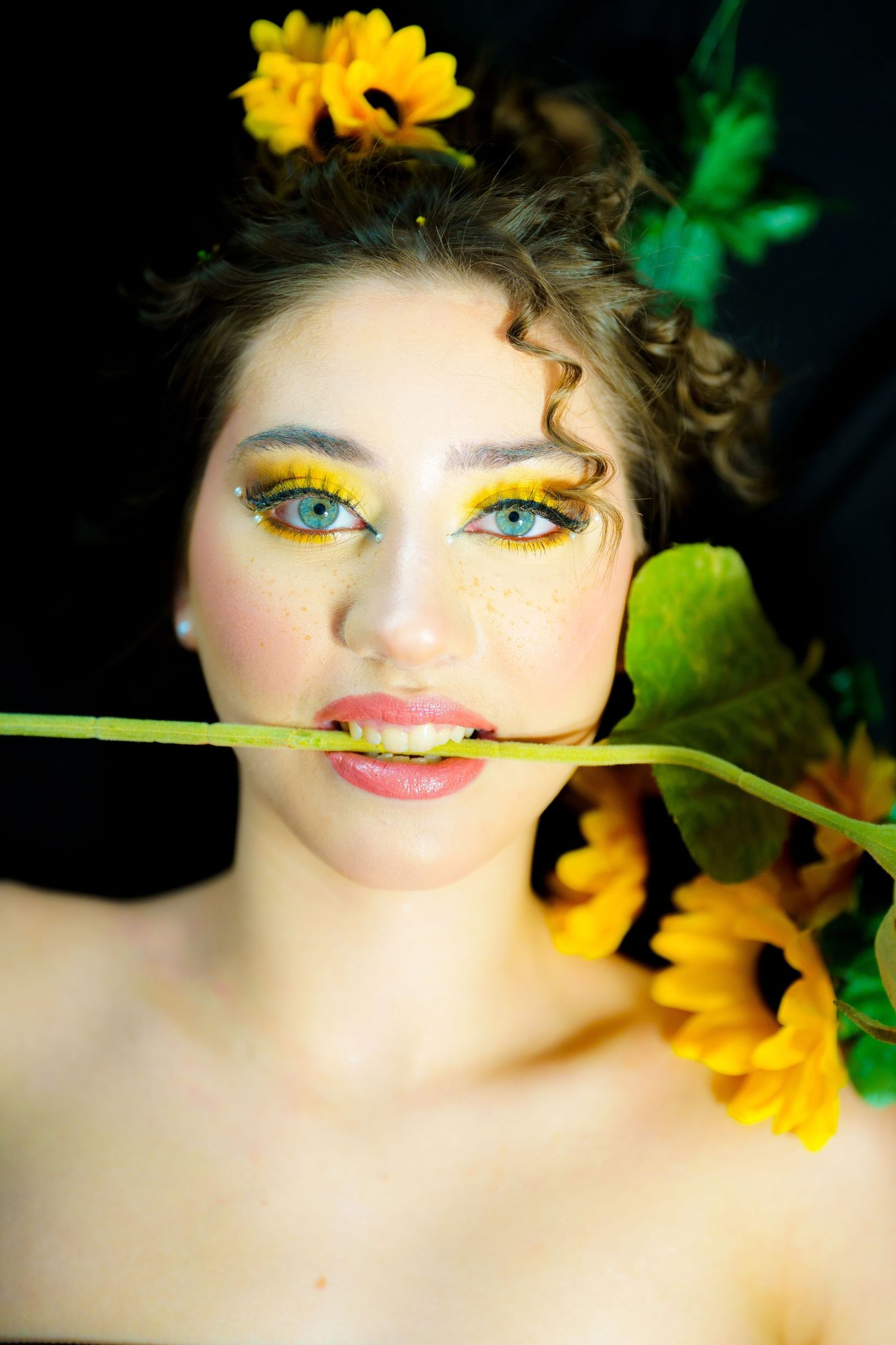Creative beauty portrait with bright yellow eyeshadow makeup and sunflowers against dark background.