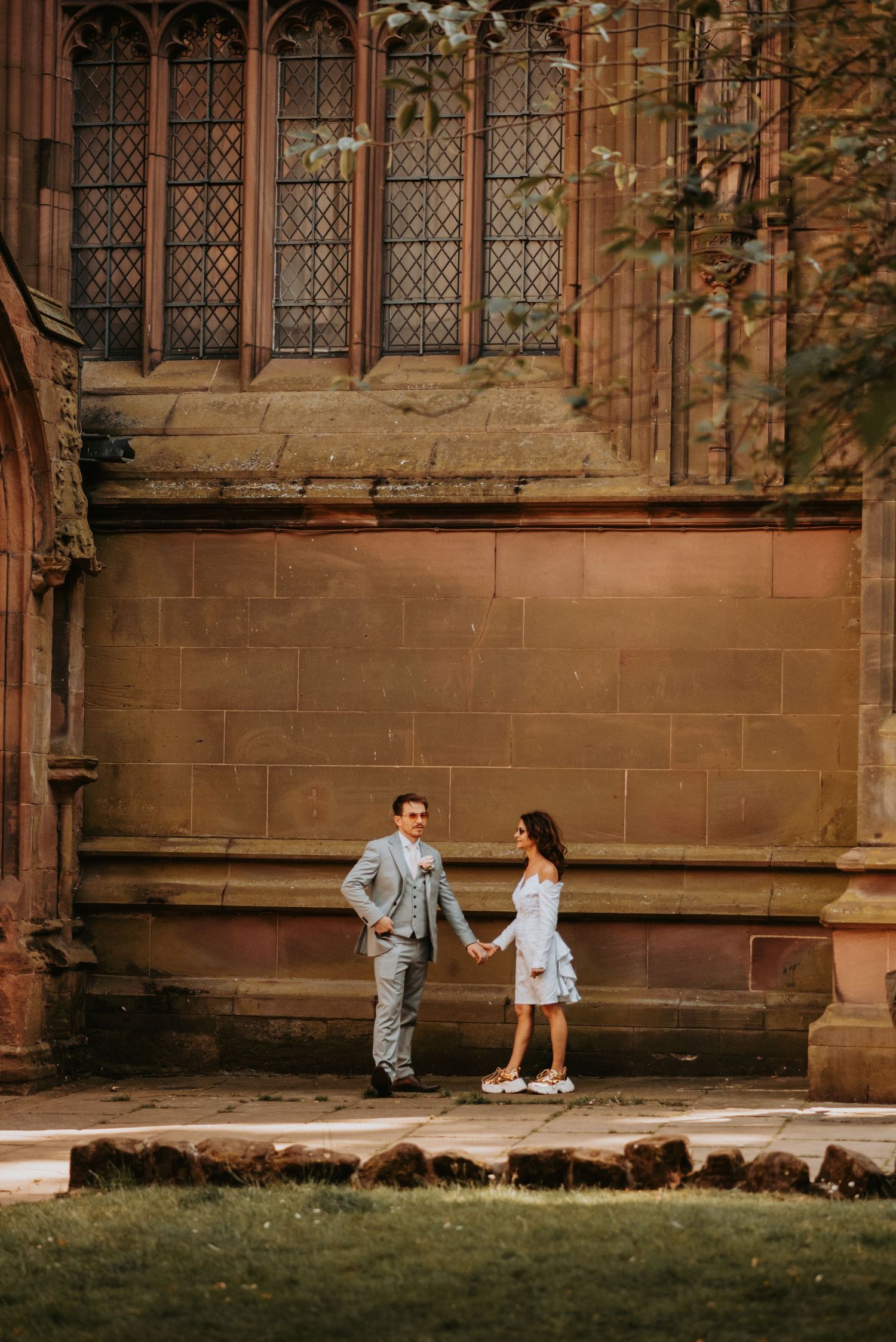 A couple stands together outside a historic stone church with gothic windows and architecture in warm evening light.