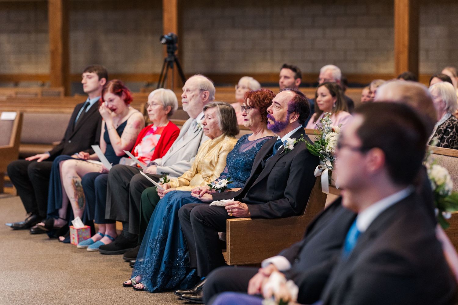 Audience members sit attentively in wooden pews during a presentation in an auditorium setting.