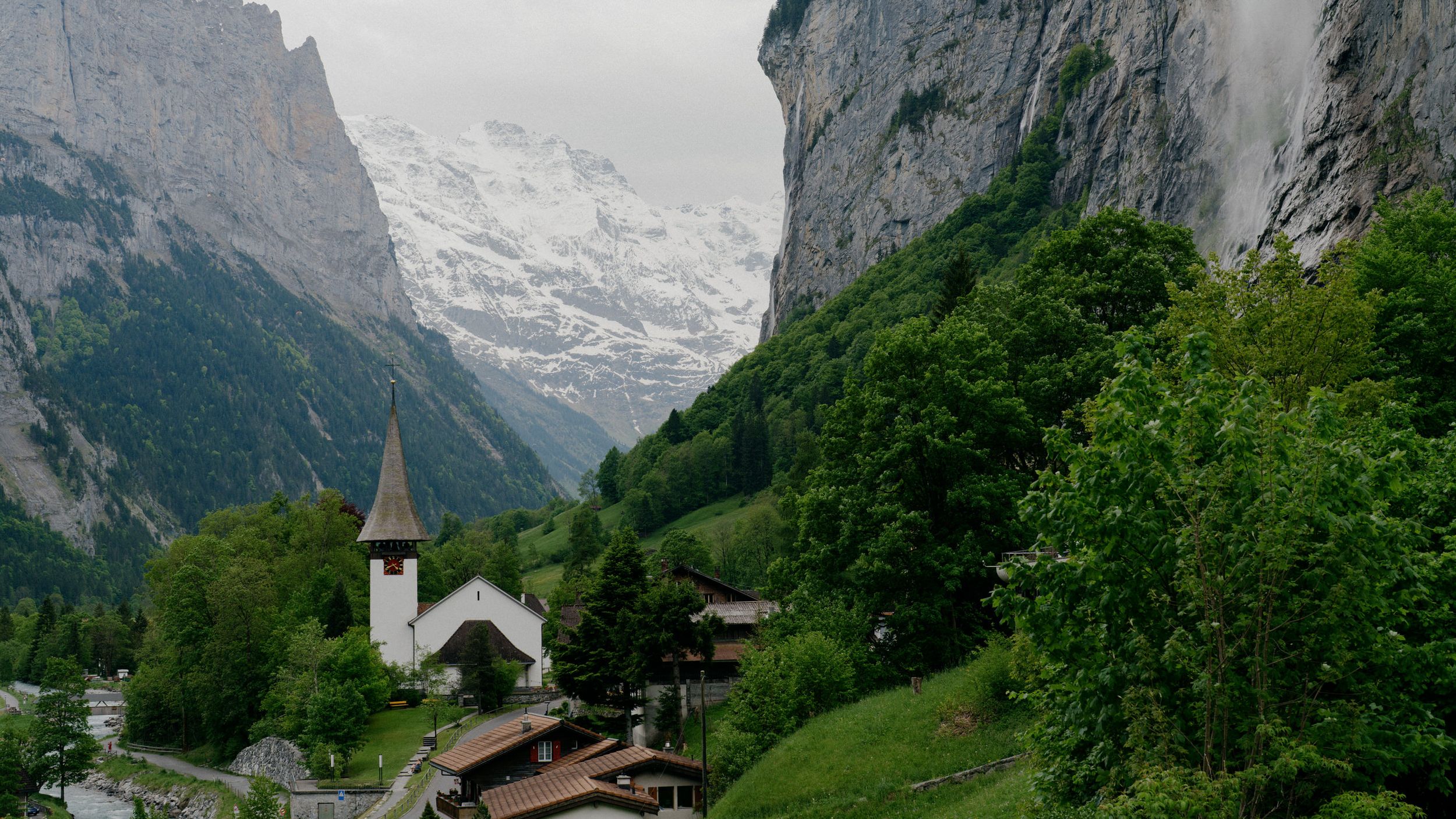 White church with tall spire nestled in lush green valley beneath towering Swiss Alps mountains in Lauterbrunnen.