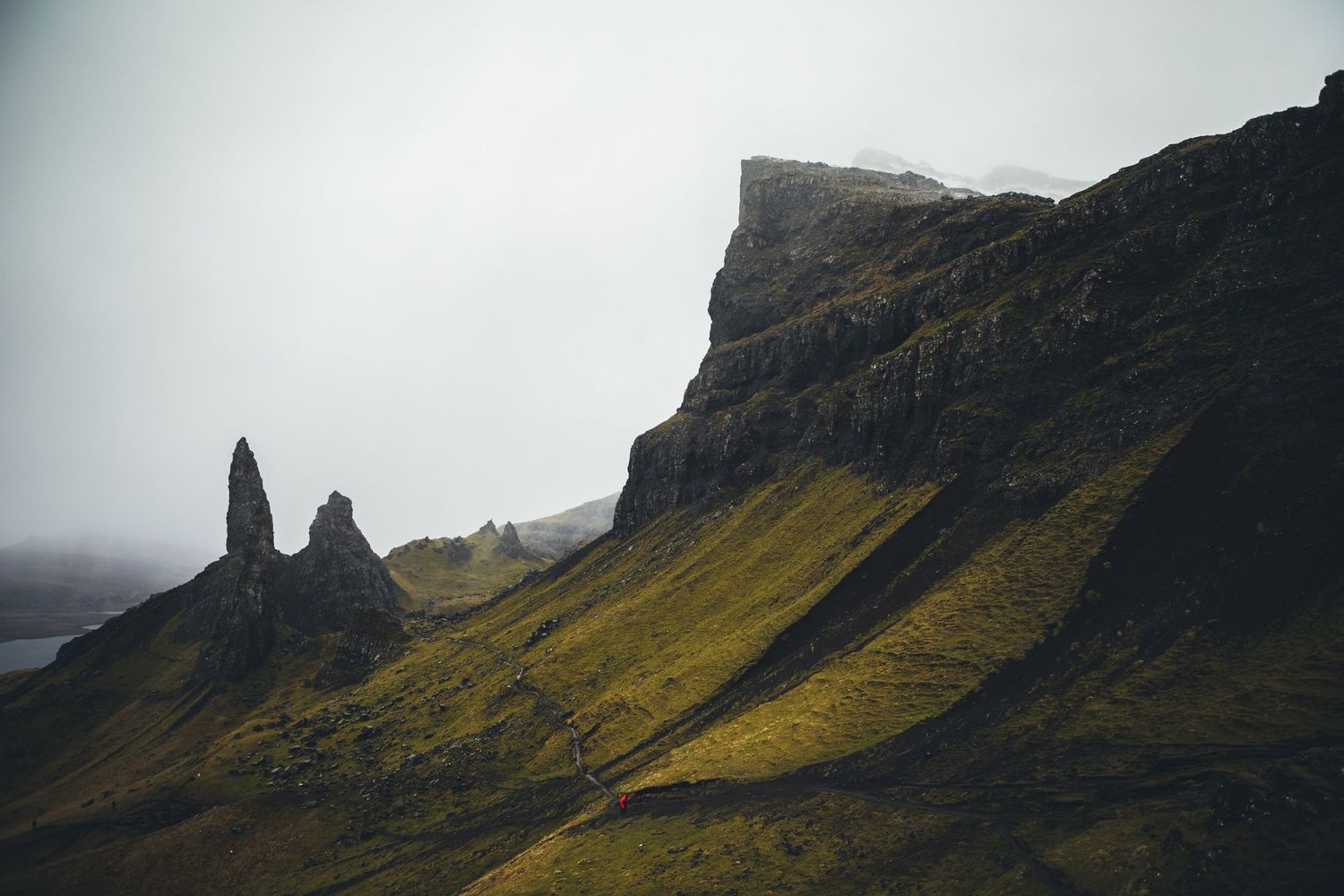 Dramatic cliffs of the Quiraing on Isle of Skye rise through fog in moody lighting.