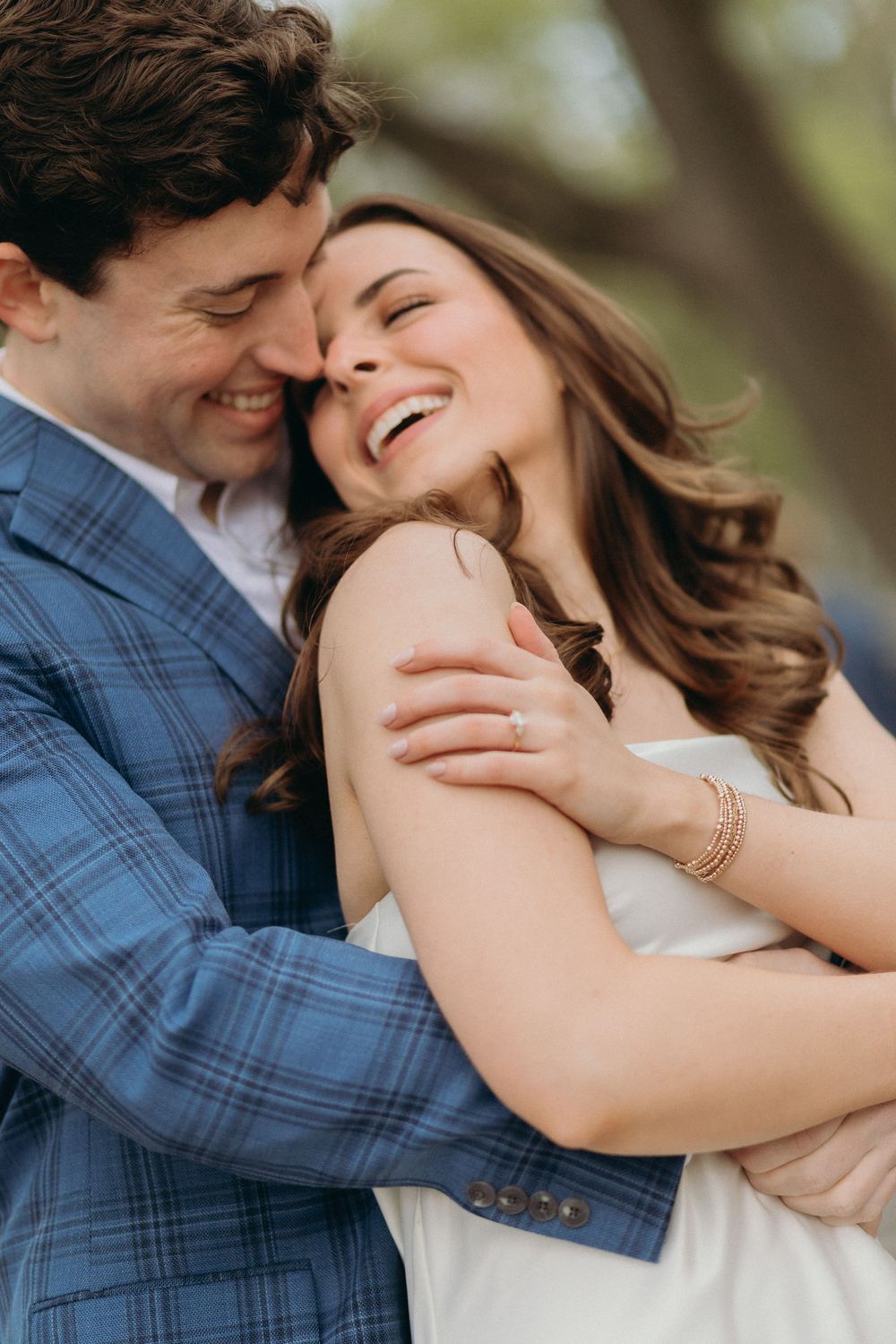 A joyful couple shares an intimate moment outdoors, with the woman laughing while wearing a white dress.