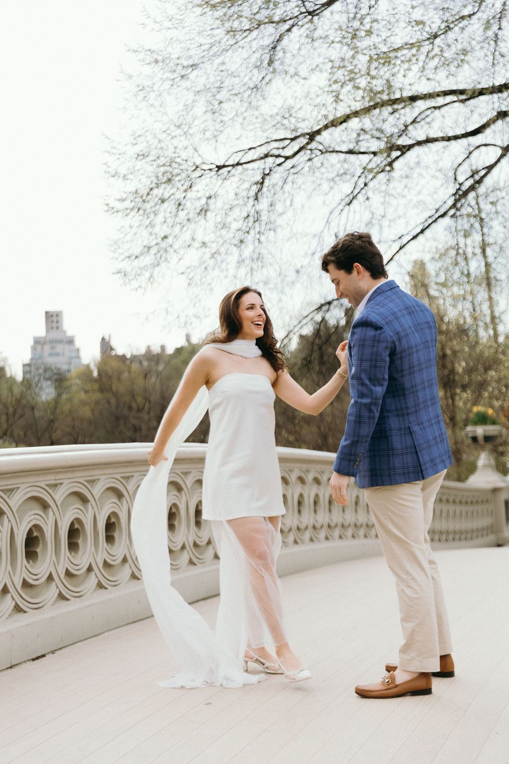 Romantic couple dancing along an ornate stone bridge railing during a photoshoot.