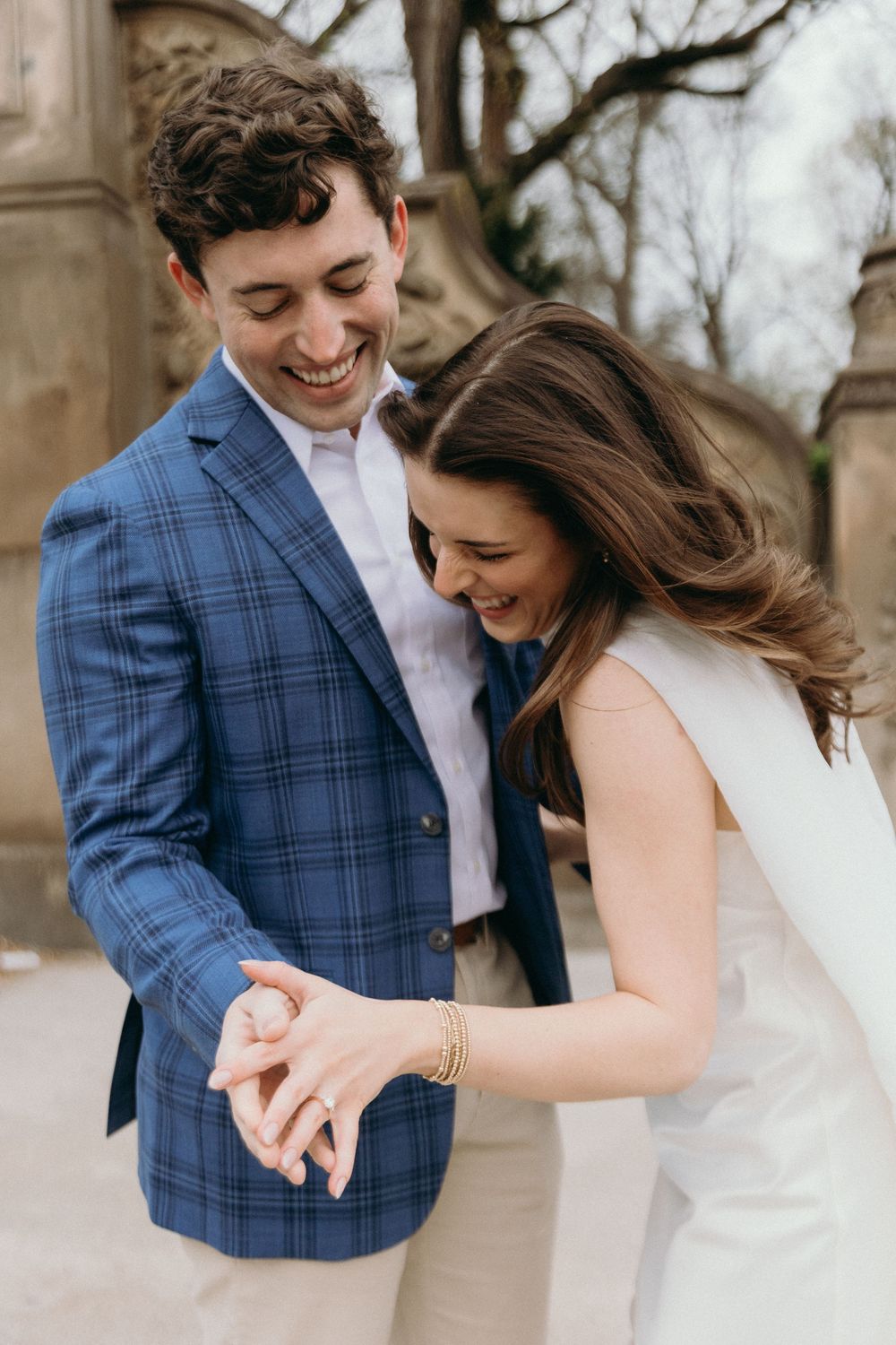 Joyful couple shares a candid laughing moment while admiring an engagement ring on the bridge.