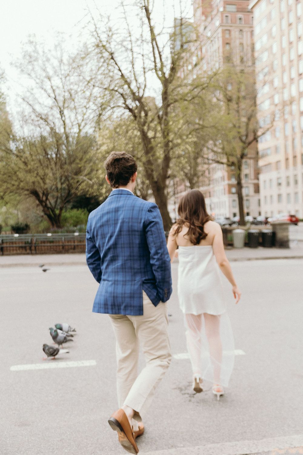 Couple in coordinated blue and white outfits walking together in an urban park with pigeons nearby.
