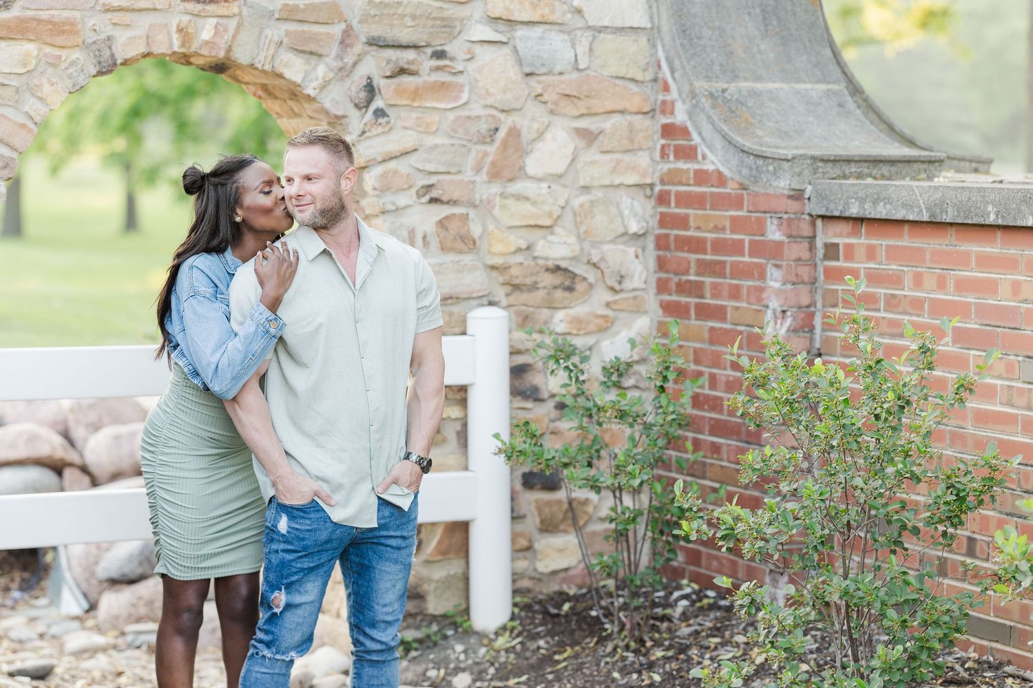 A couple shares an intimate moment together while standing next to a stone and brick wall outdoors.