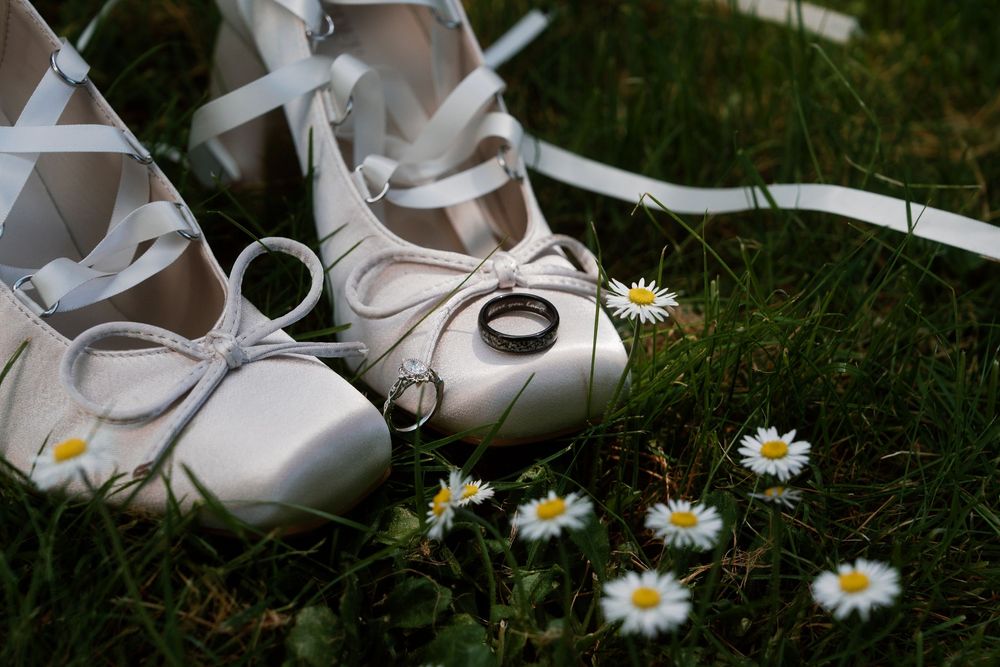 White ballet pointe shoes resting on green grass next to delicate white daisies in a dreamy summer scene.