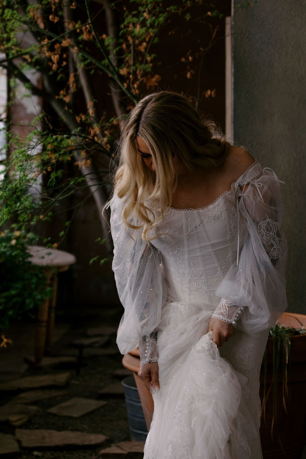A bride in a delicate white lace wedding dress with billowing sleeves poses in a garden setting.