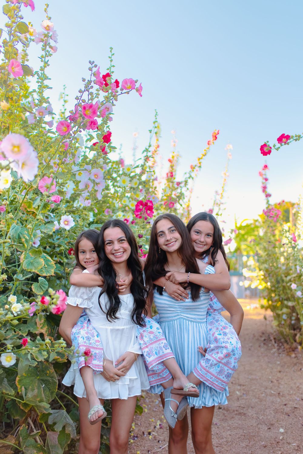 A group of friends in coordinating blue and white outfits pose together among flowering bushes at sunset.