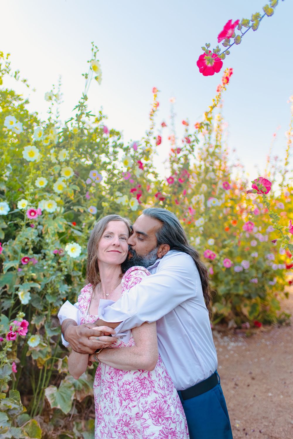 A romantic couple embraces in a garden with vibrant pink hollyhocks at an Arizona flower farm.