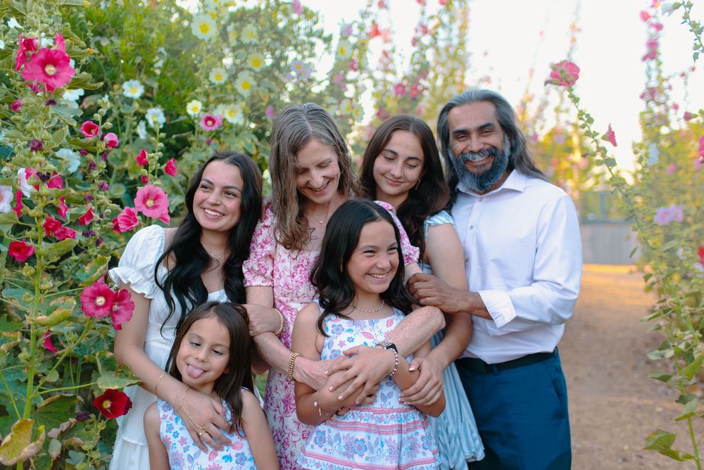 Family group dressed in white and pink poses together along a path lined with blooming spring hollyhocks.
