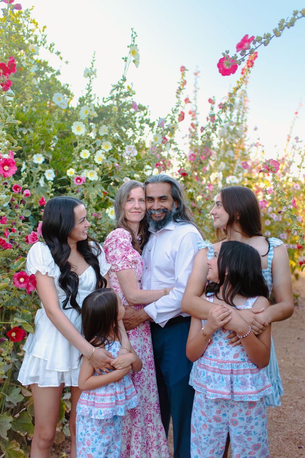 A family shares a joyful moment together in a garden with blooming pink hollyhock flowers on a sunny day.
