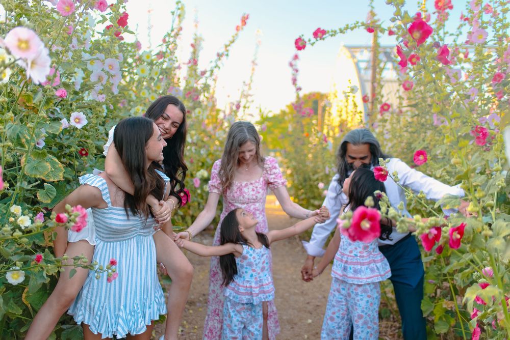 A joyful family explores a vibrant pink floral garden together during a sunset photoshoot session.