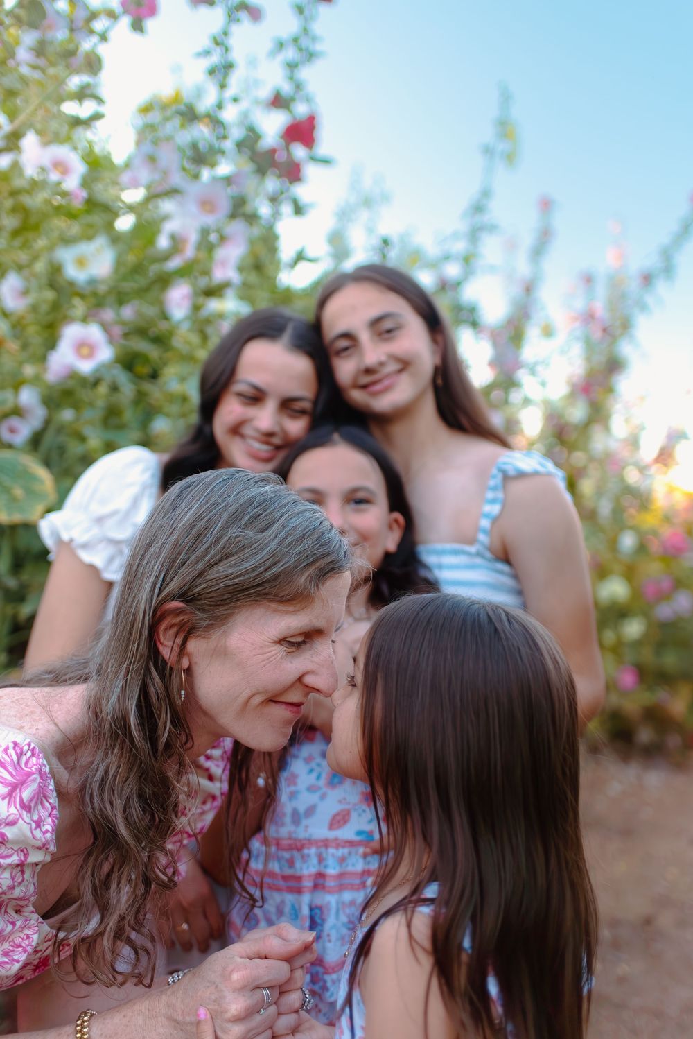 A family laughing together outdoors with pink flowers in the background on a sunny afternoon.