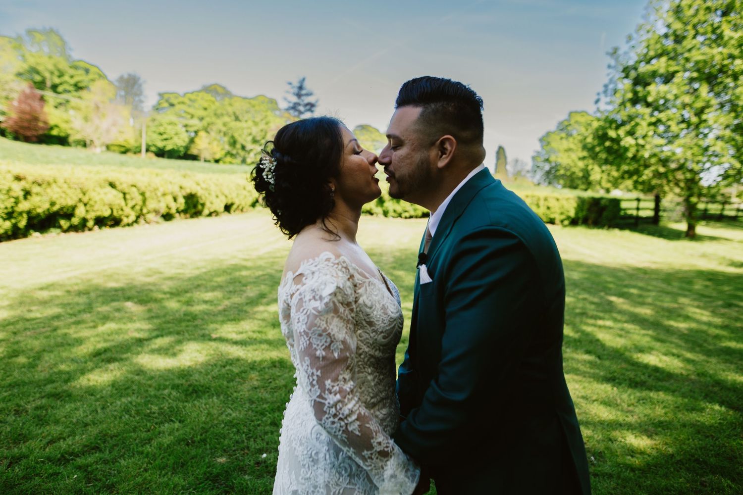 A couple shares a romantic moment together in a sunlit green park setting during a wedding celebration.