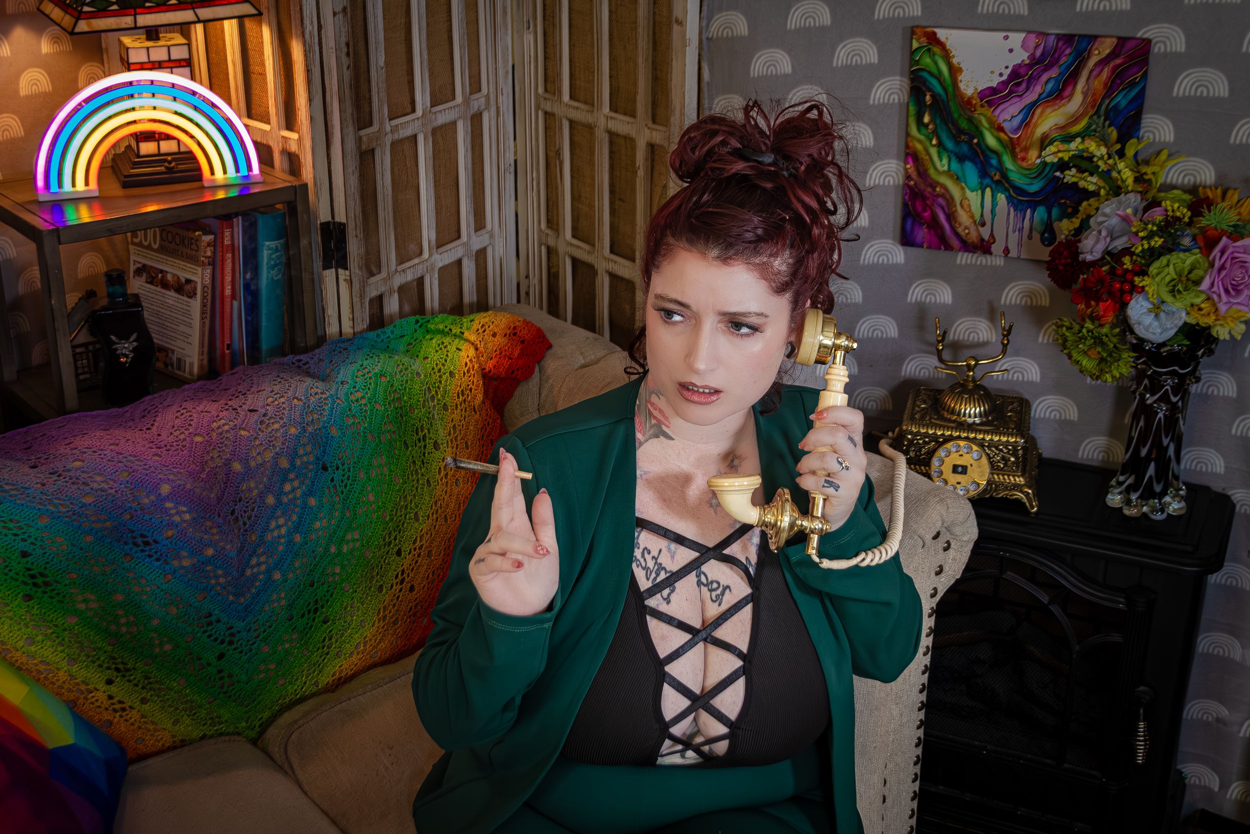 Person in green blazer and black bra poses with vintage telephone and a joint in a room with rainbow lighting and colorful decor.