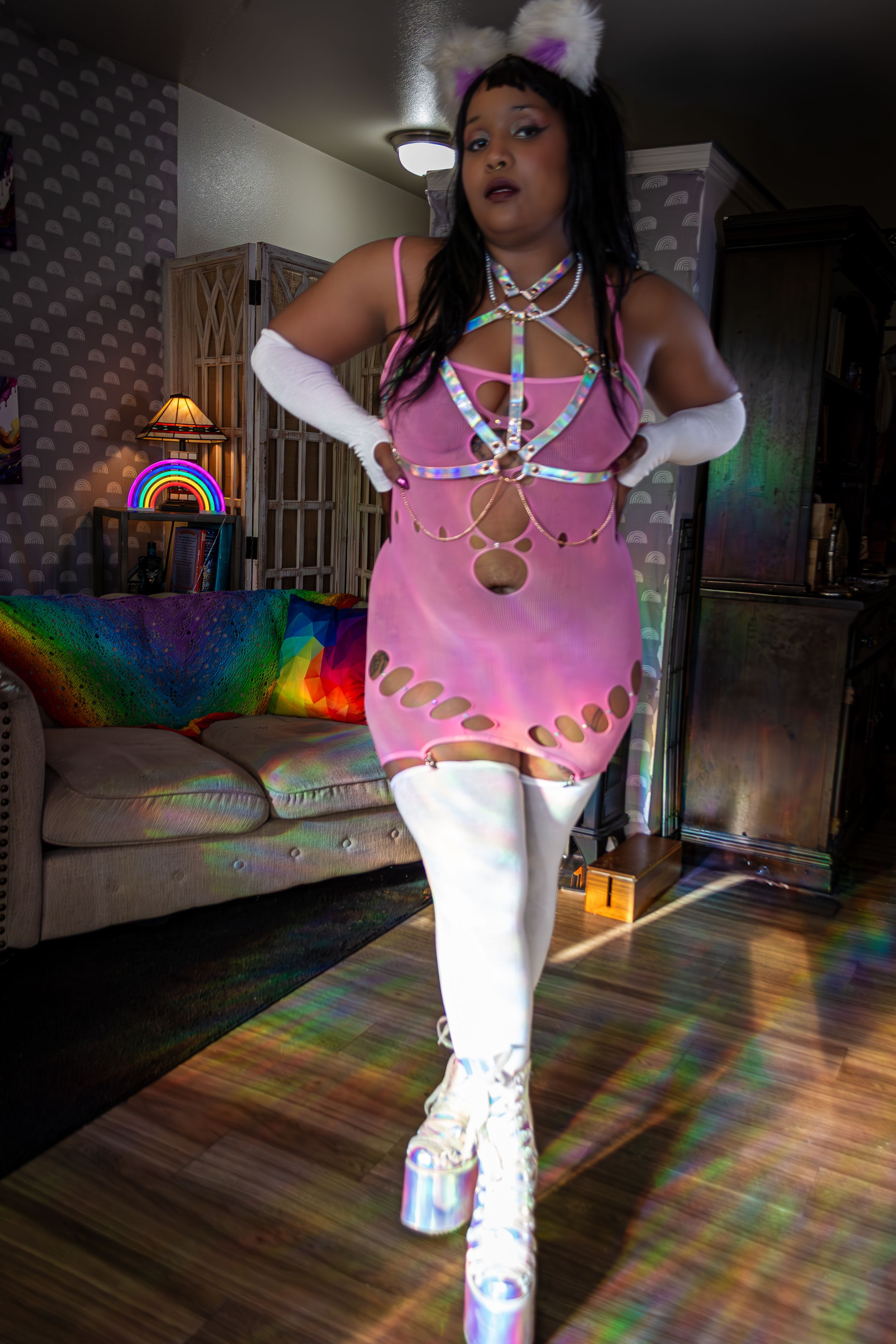 A person wearing a pink and white costume strikes different dance poses on a floor illuminated with rainbow light effects.