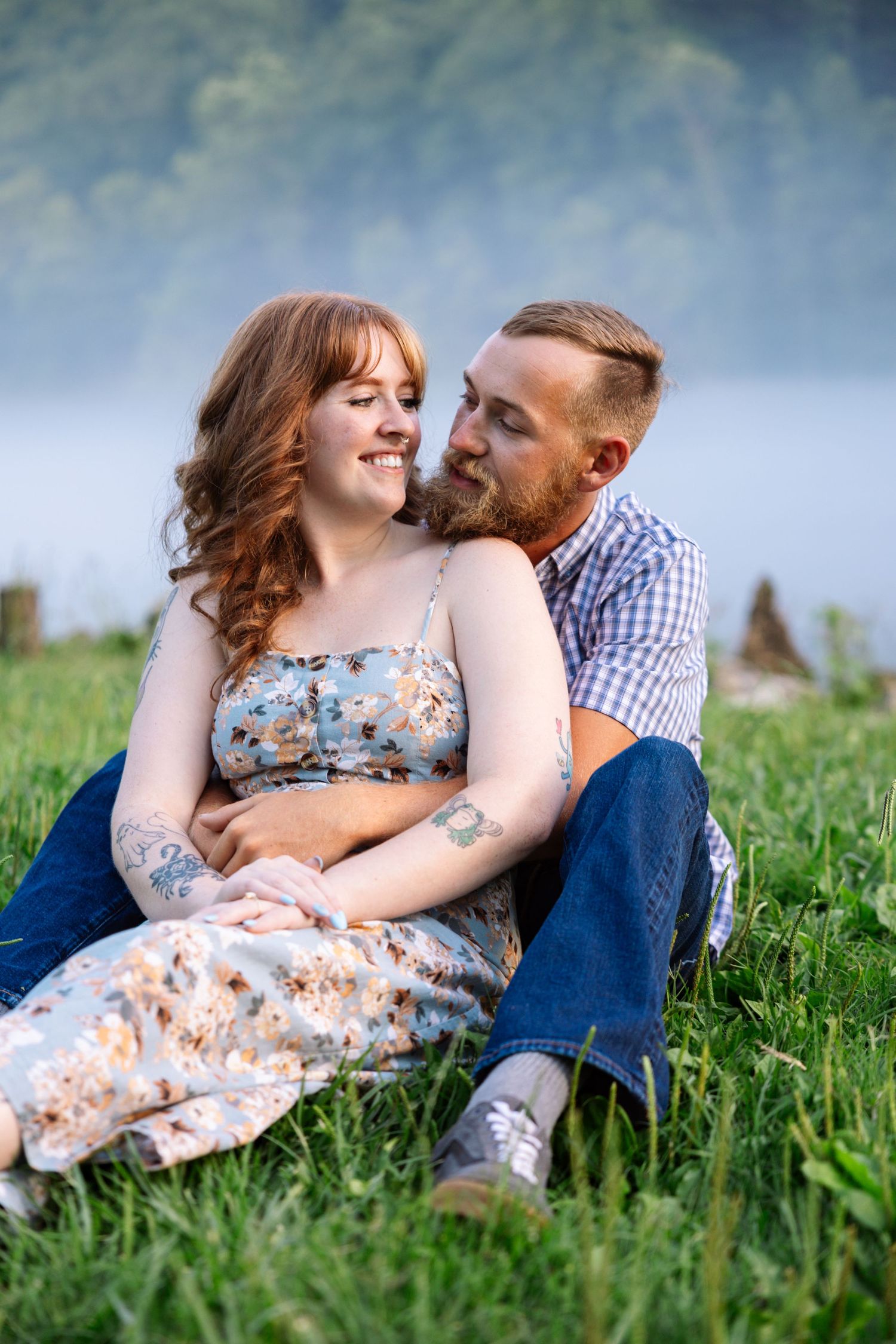 Romantic couple sitting together in green grass meadow during foggy weather while wearing casual summer attire. Norris Dam.