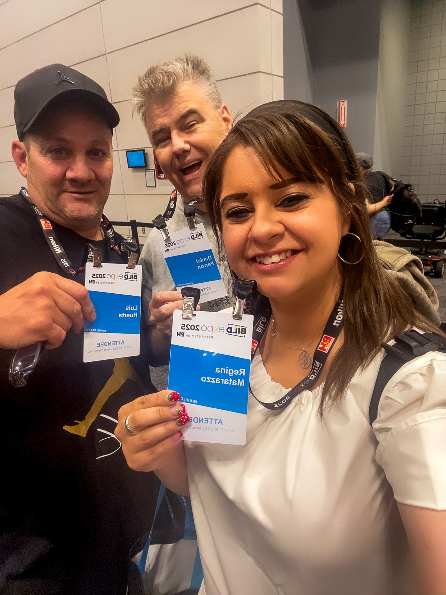 Three people showing their conference name badges and smiling together at an event hallway.
