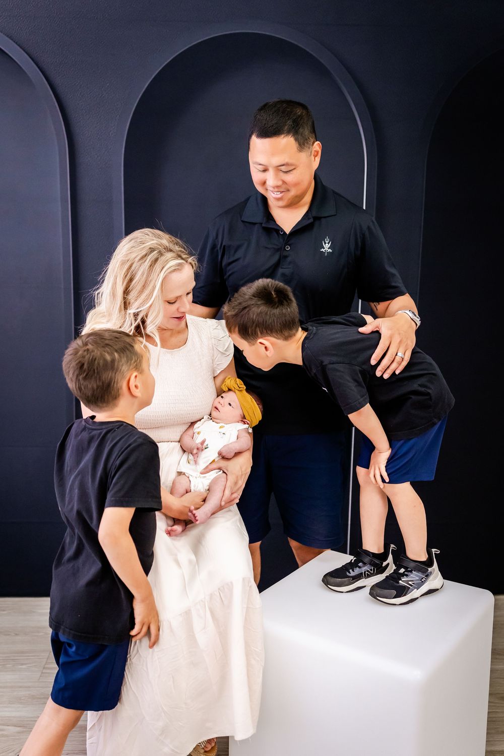 Family members gather around while young children interact with a baby in a white dress.