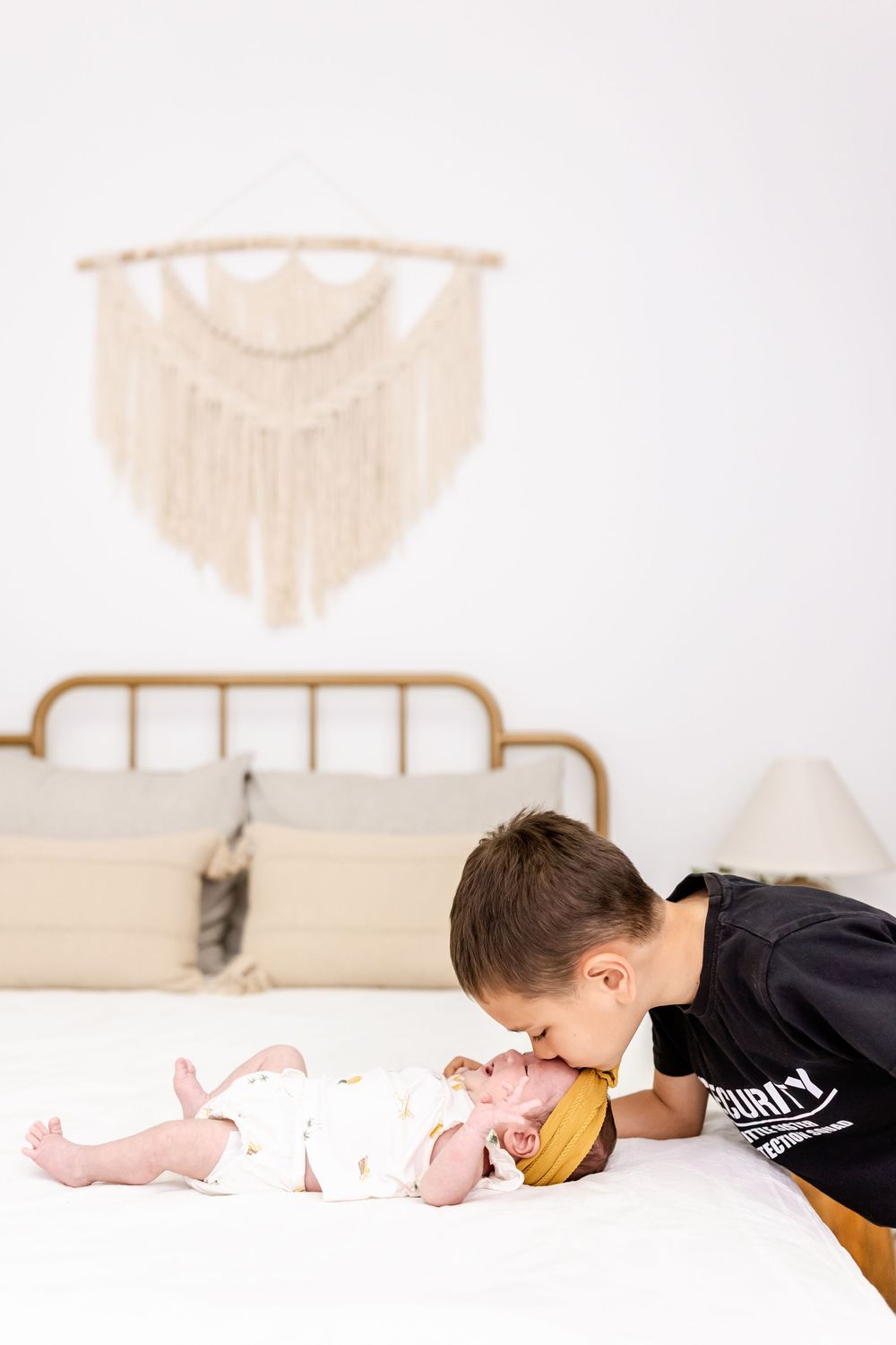 Children lying on a white bed interacting with a baby in a bright, airy setting.