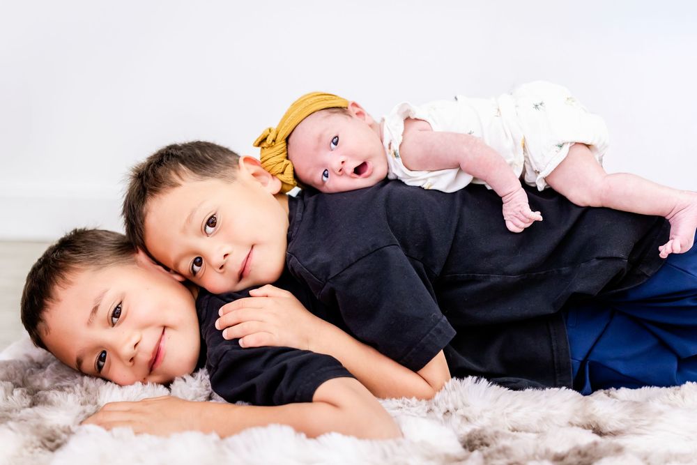 Baby in a yellow headband lying on fluffy white fabric while being held by an adult wearing black.