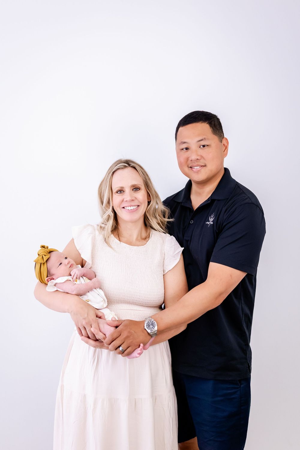 Family of three poses together for a portrait against a white backdrop.