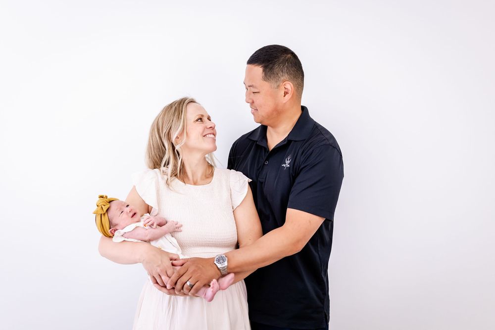 A family poses together while holding a baby against a white studio backdrop.