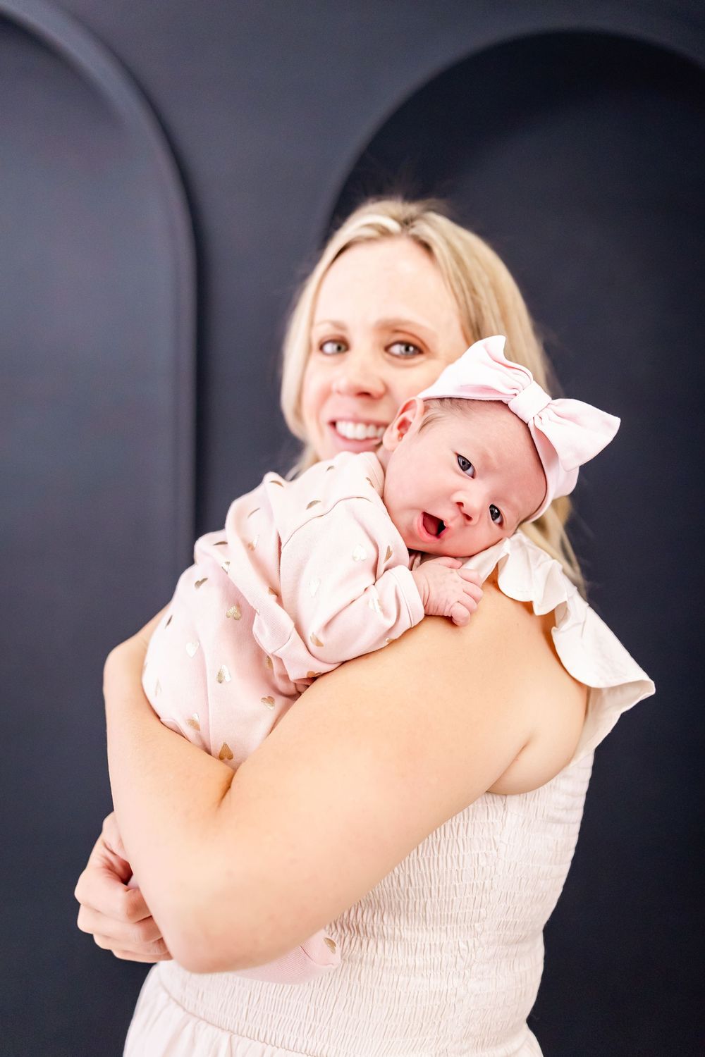 A series of photos showing a baby in pink clothing being held against a dark background.